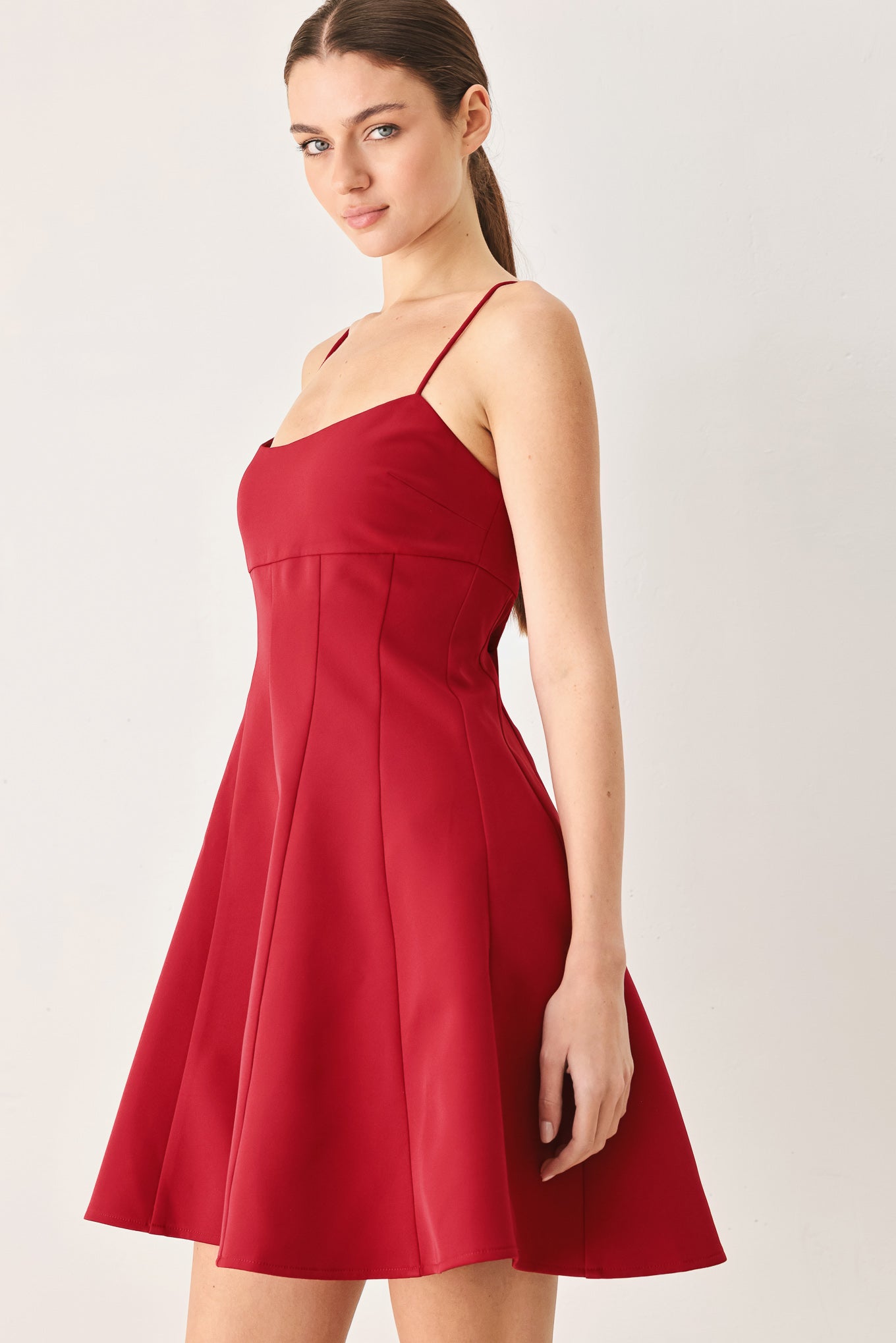 A woman wearing a red spaghetti-strap mini dress with a structured bodice and flared skirt | Flying Tomato