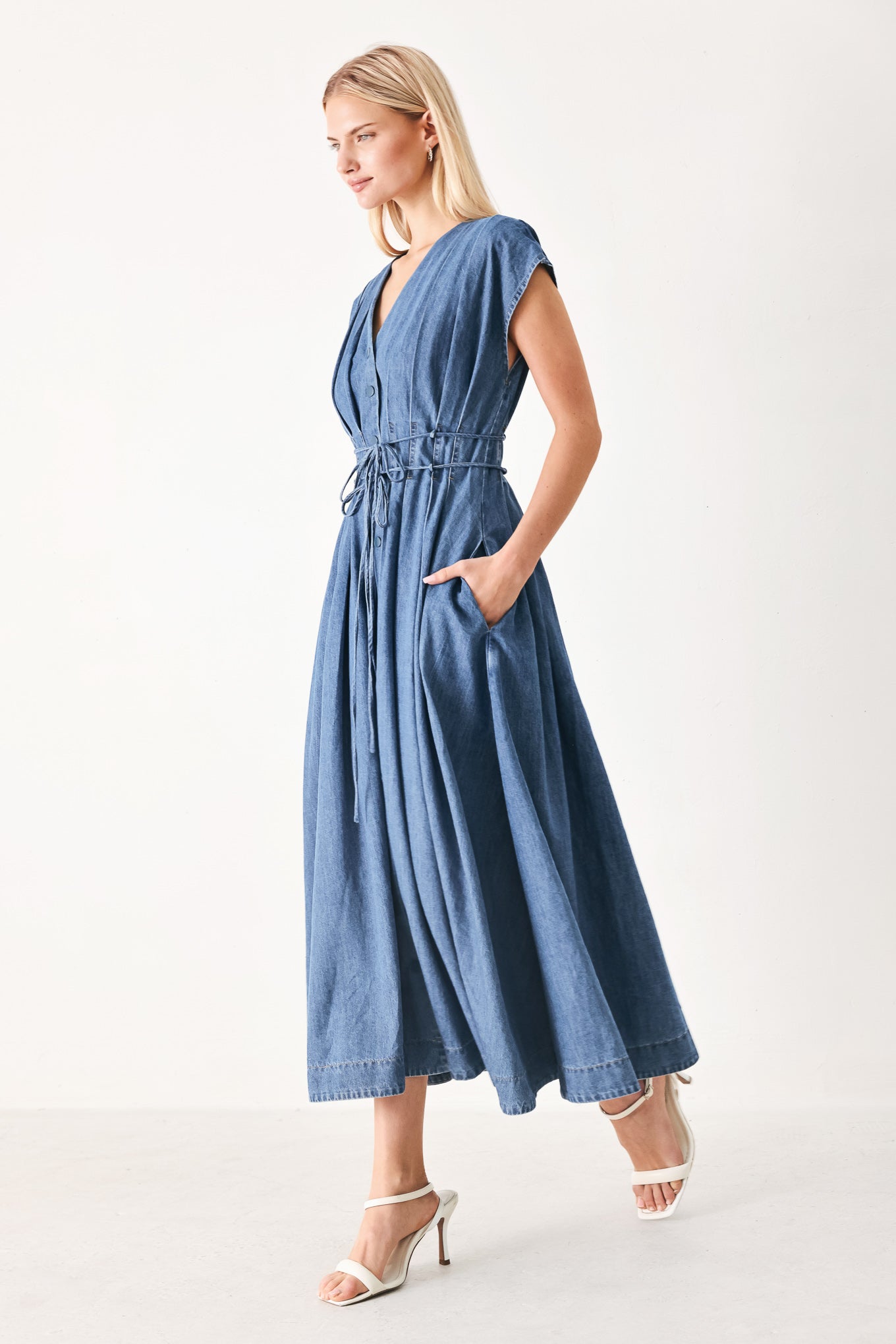 Woman wearing a blue denim midi dress featuring V neckline, drop shoulder, corset waist with pleats, double tie and full skirt | FREEMARKET