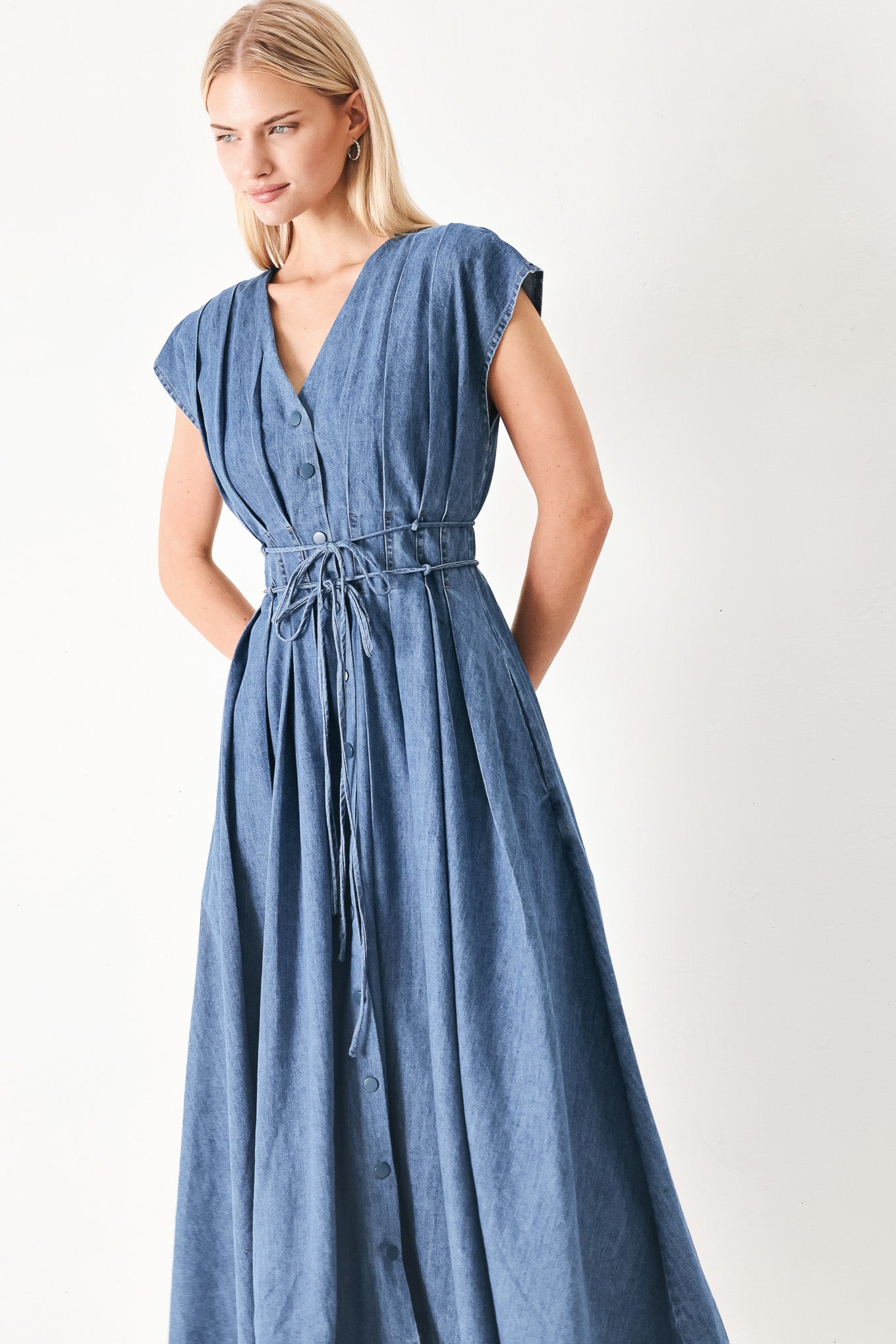 Woman wearing a blue denim midi dress featuring V neckline, drop shoulder, corset waist with pleats, double tie and full skirt | FREEMARKET