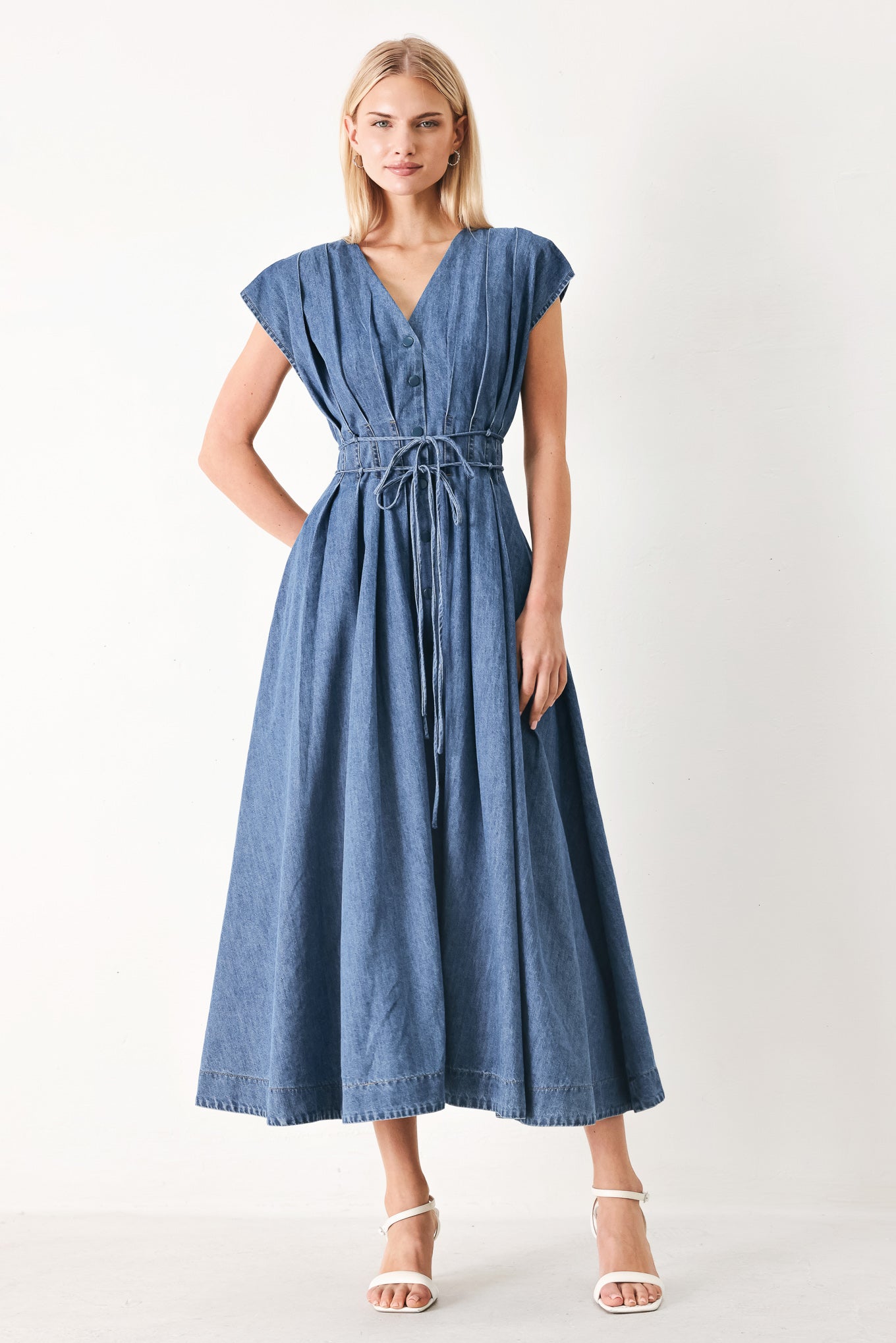 Woman wearing a blue denim midi dress featuring V neckline, drop shoulder, corset waist with pleats, double tie and full skirt | FREEMARKET