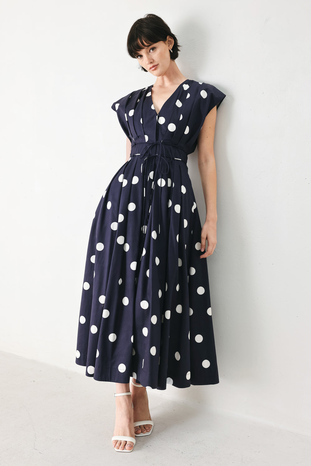 Woman wearing a navy blue midi dress with white polka dots featuring V neckline, short sleeve, front button, corset waist, double tie and full skirt | FREEMARKET