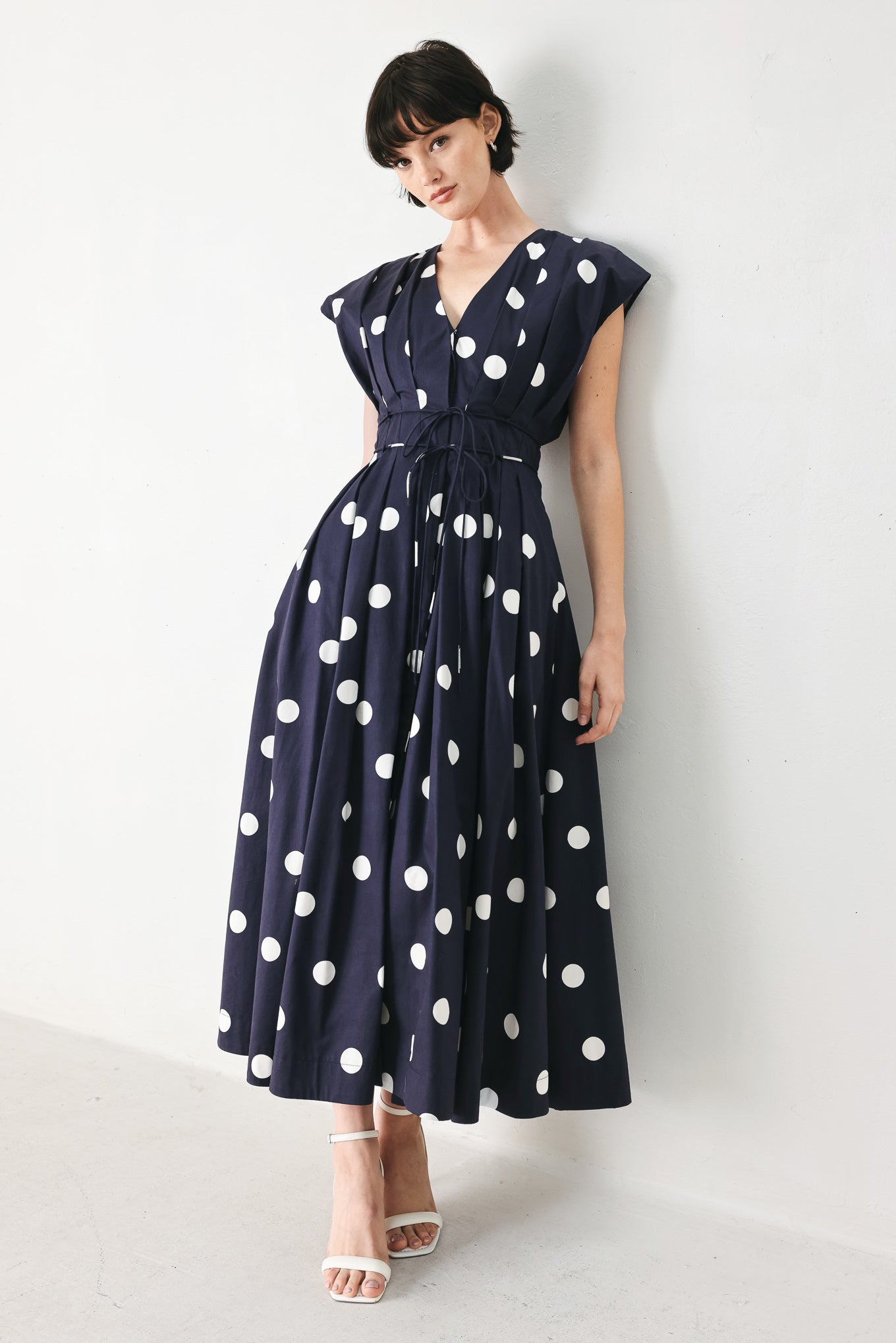 Woman wearing a navy blue midi dress with white polka dots featuring V neckline, short sleeve, front button, corset waist, double tie and full skirt | FREEMARKET