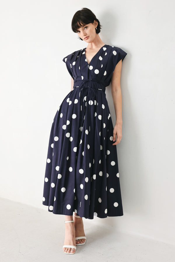 Woman wearing a navy blue midi dress with white polka dots featuring V neckline, short sleeve, front button, corset waist, double tie and full skirt | FREEMARKET