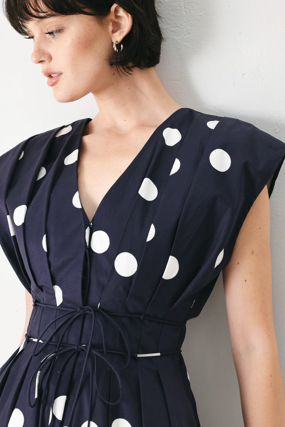Woman wearing a navy blue midi dress with white polka dots featuring V neckline, short sleeve, front button, corset waist, double tie and full skirt | FREEMARKET