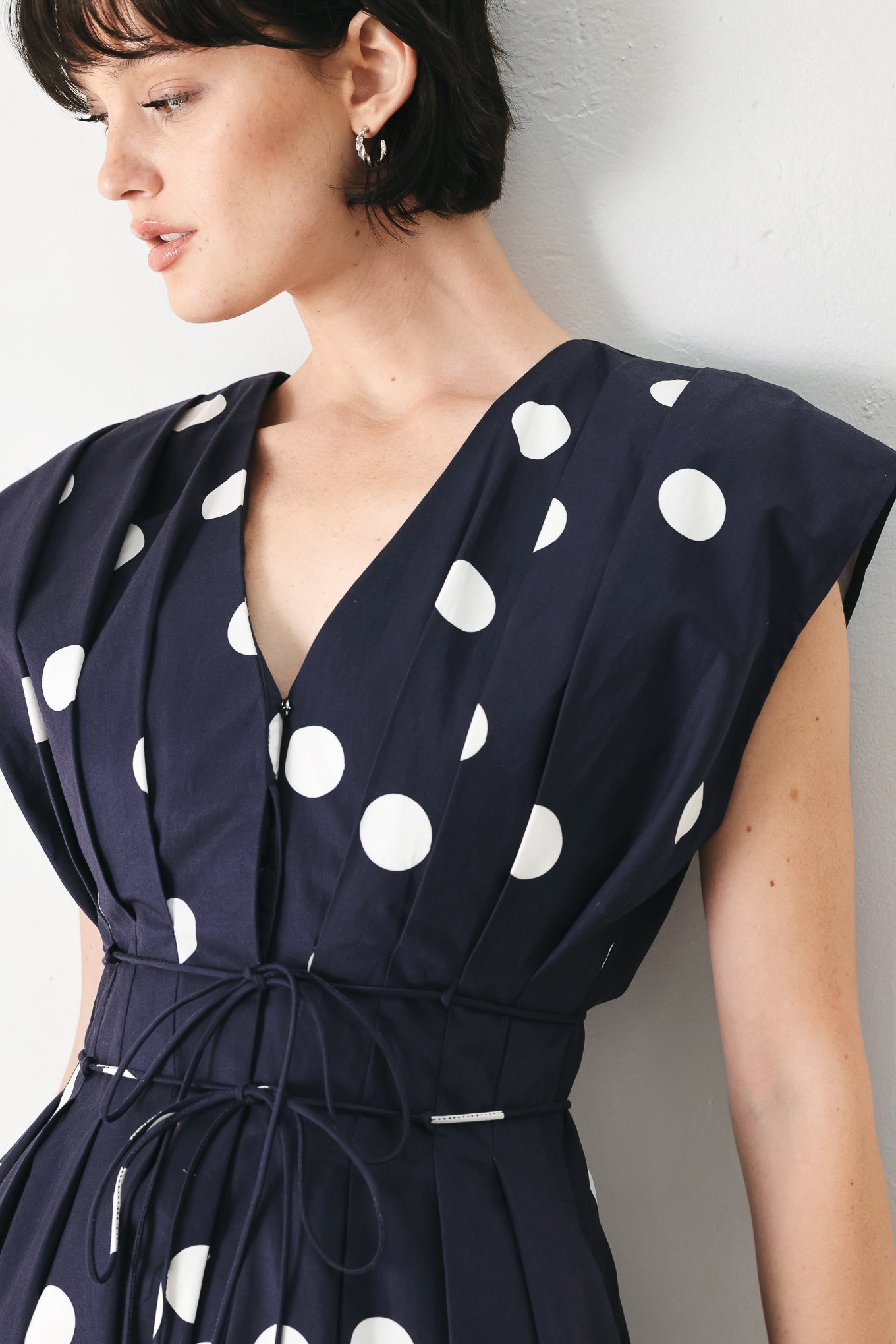 Woman wearing a navy blue midi dress with white polka dots featuring V neckline, short sleeve, front button, corset waist, double tie and full skirt | FREEMARKET