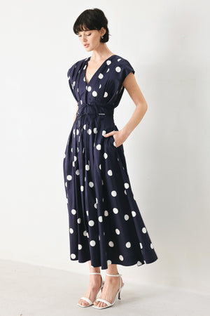 Woman wearing a navy blue midi dress with white polka dots featuring V neckline, short sleeve, front button, corset waist, double tie and full skirt | FREEMARKET