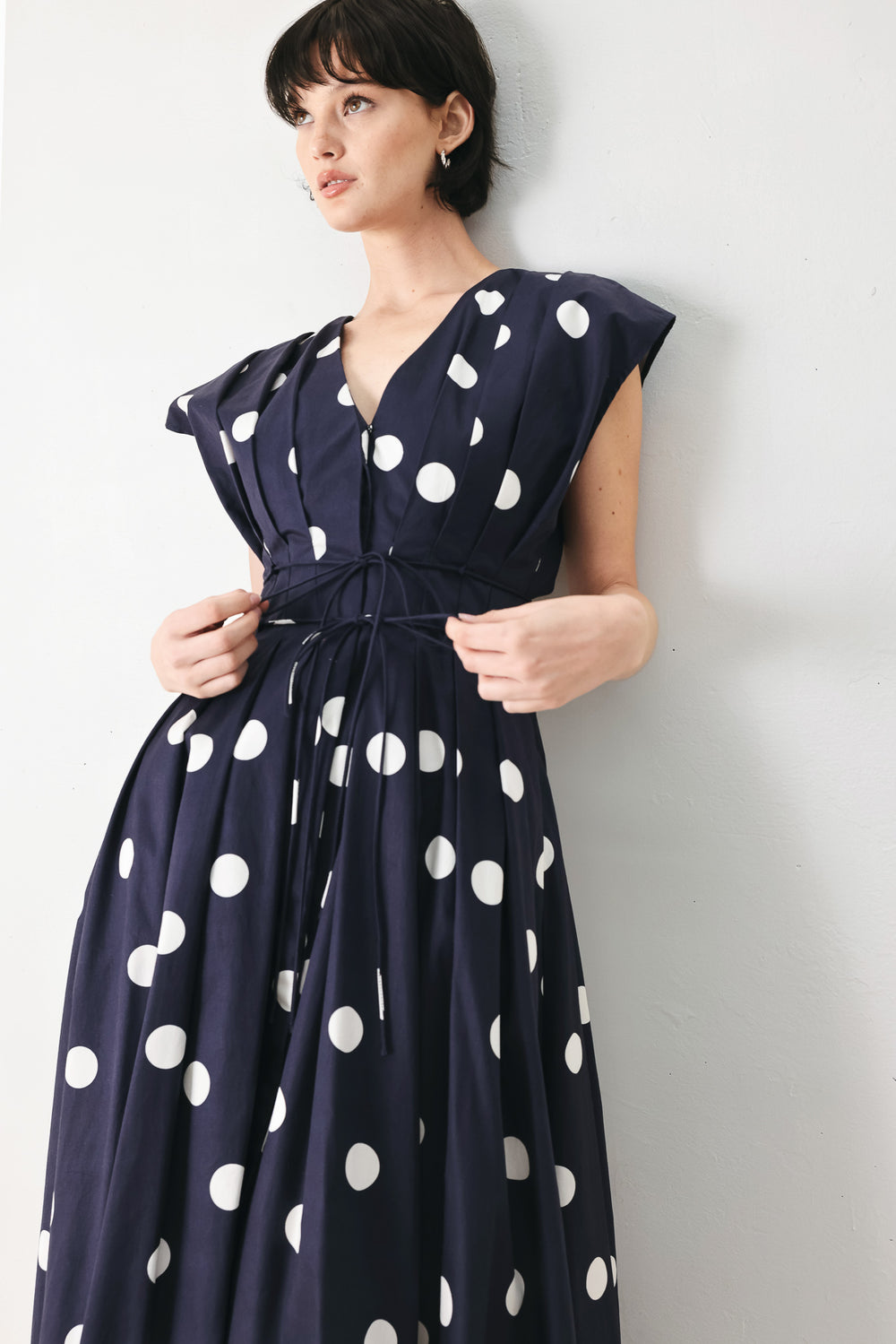 Woman wearing a navy blue midi dress with white polka dots featuring V neckline, short sleeve, front button, corset waist, double tie and full skirt | FREEMARKET