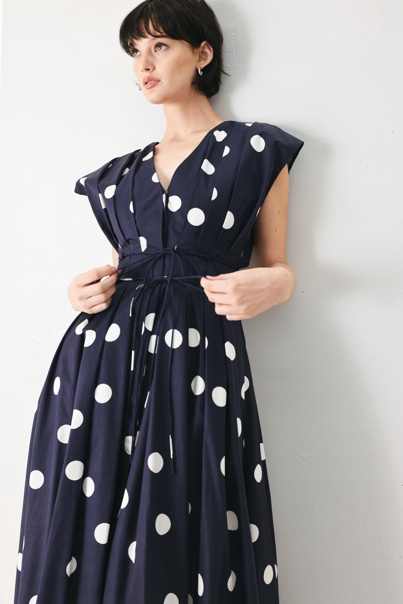 Woman wearing a navy blue midi dress with white polka dots featuring V neckline, short sleeve, front button, corset waist, double tie and full skirt | FREEMARKET