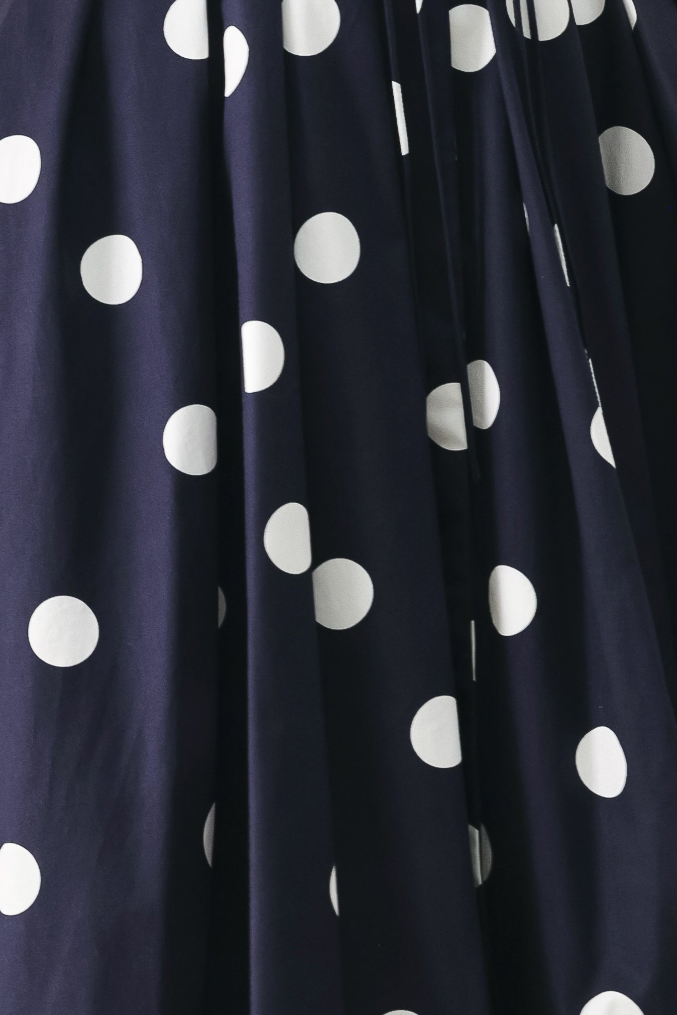 Close up of a navy blue midi dress with white polka dots featuring V neckline, short sleeve, front button, corset waist, double tie and full skirt | FREEMARKET
