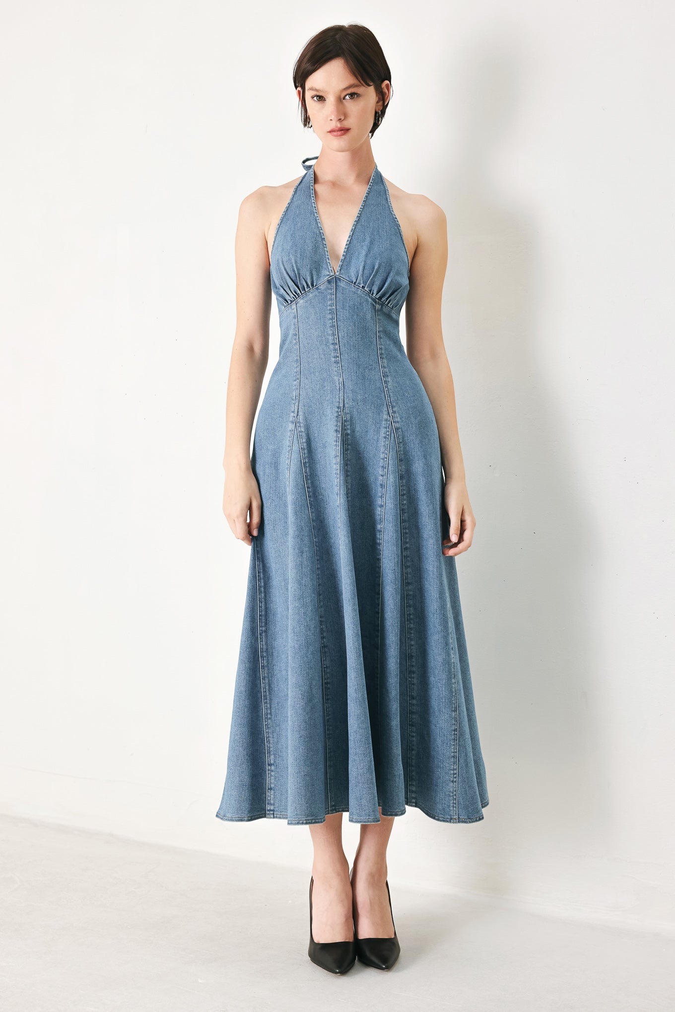 A washed denim midi dress featuring halter neckline with back tie, full circle skirt, bare back with zipper closure