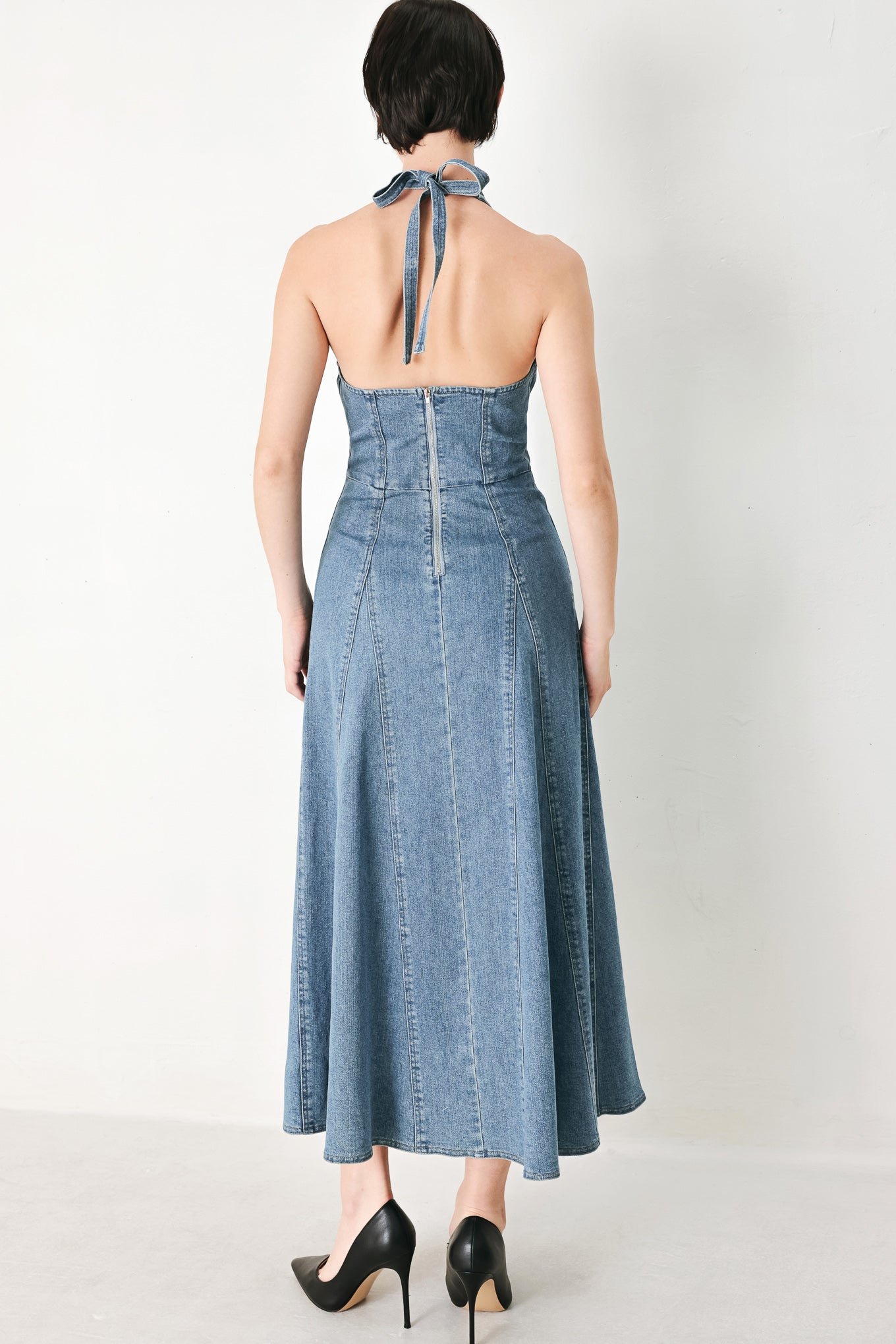 A washed denim midi dress featuring halter neckline with back tie, full circle skirt, bare back with zipper closure