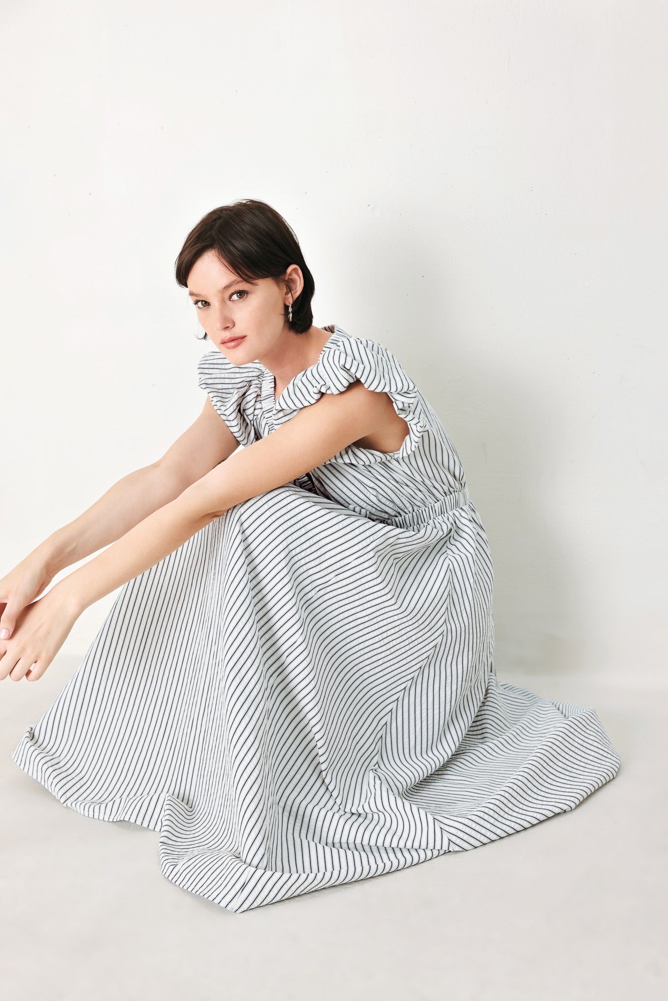 A striped woven midi dress featuring V neckline, short balloon sleeves, front tie, elastic at empire and full skirt