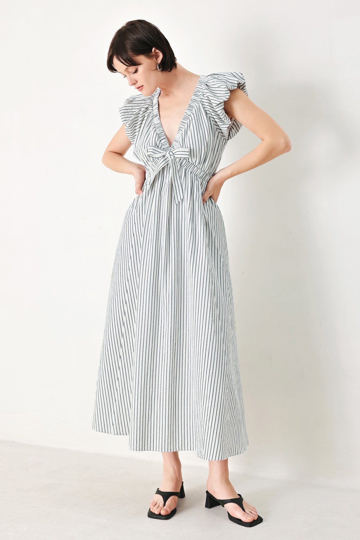 A striped woven midi dress featuring V neckline, short balloon sleeves, front tie, elastic at empire and full skirt