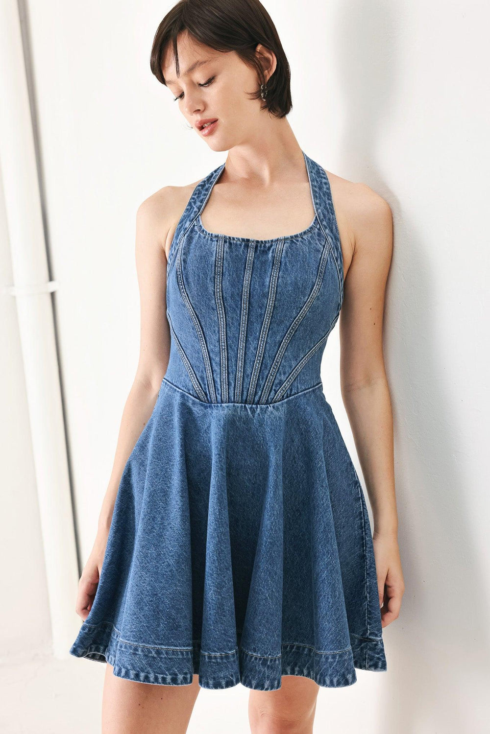 A washed denim mini dress featuring halter neckline with back button closure, full circle skirt bare back with zipper closure