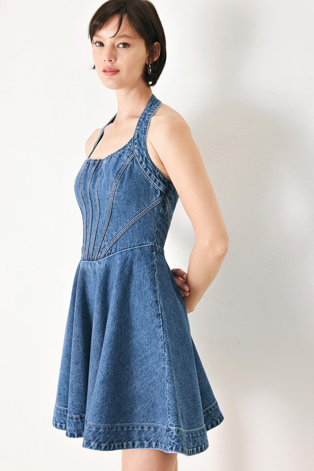 A washed denim mini dress featuring halter neckline with back button closure, full circle skirt bare back with zipper closure