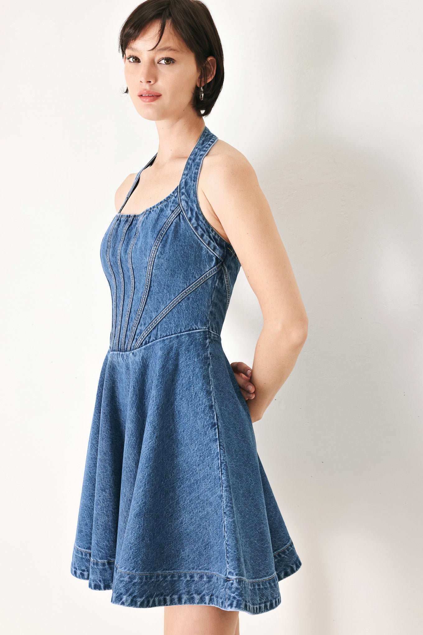 A washed denim mini dress featuring halter neckline with back button closure, full circle skirt bare back with zipper closure