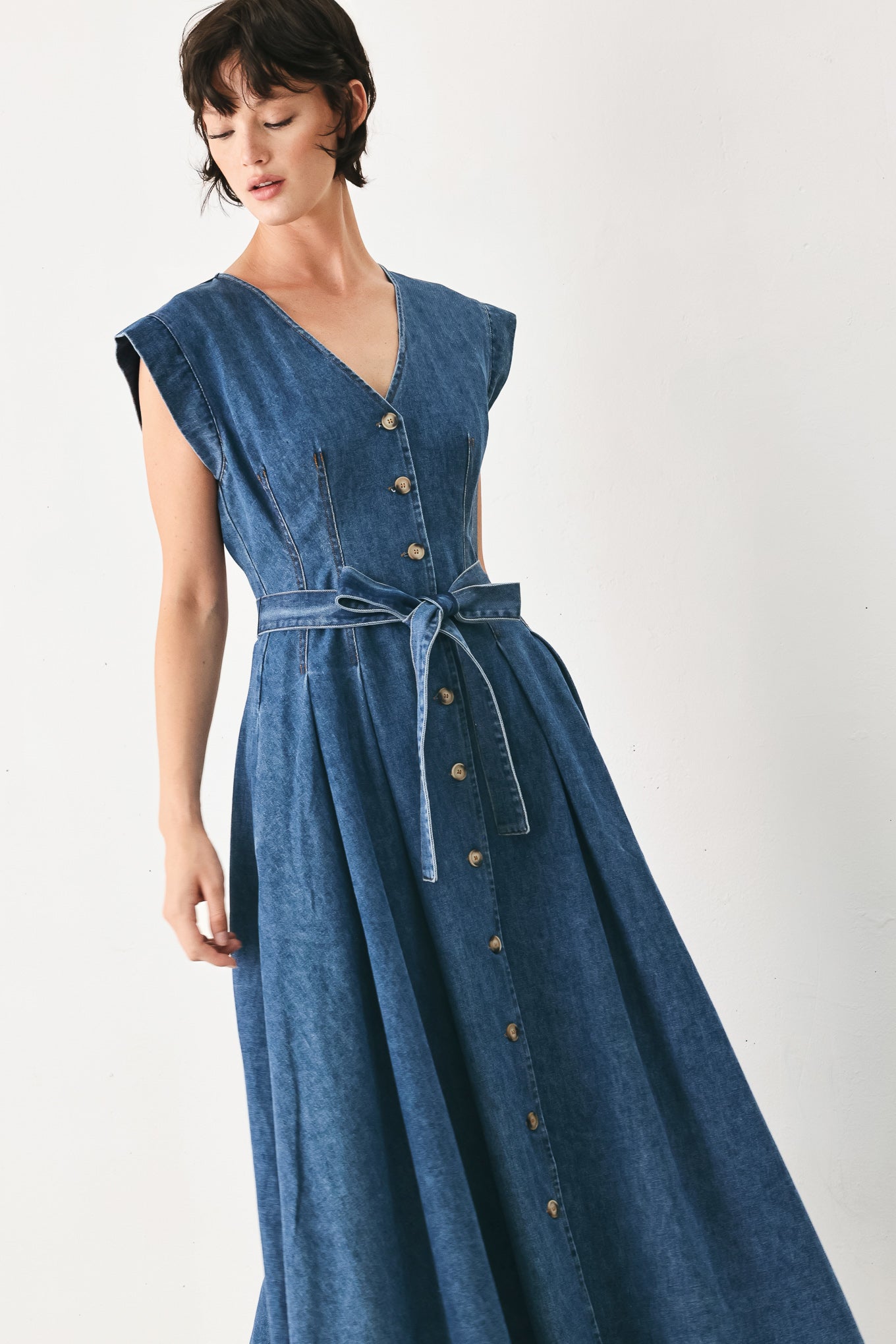 Woman wearing a short sleeve blue denim midi dress with V neckline, front button down, corset waist, self sash tie and full skirt | FREEMARKET