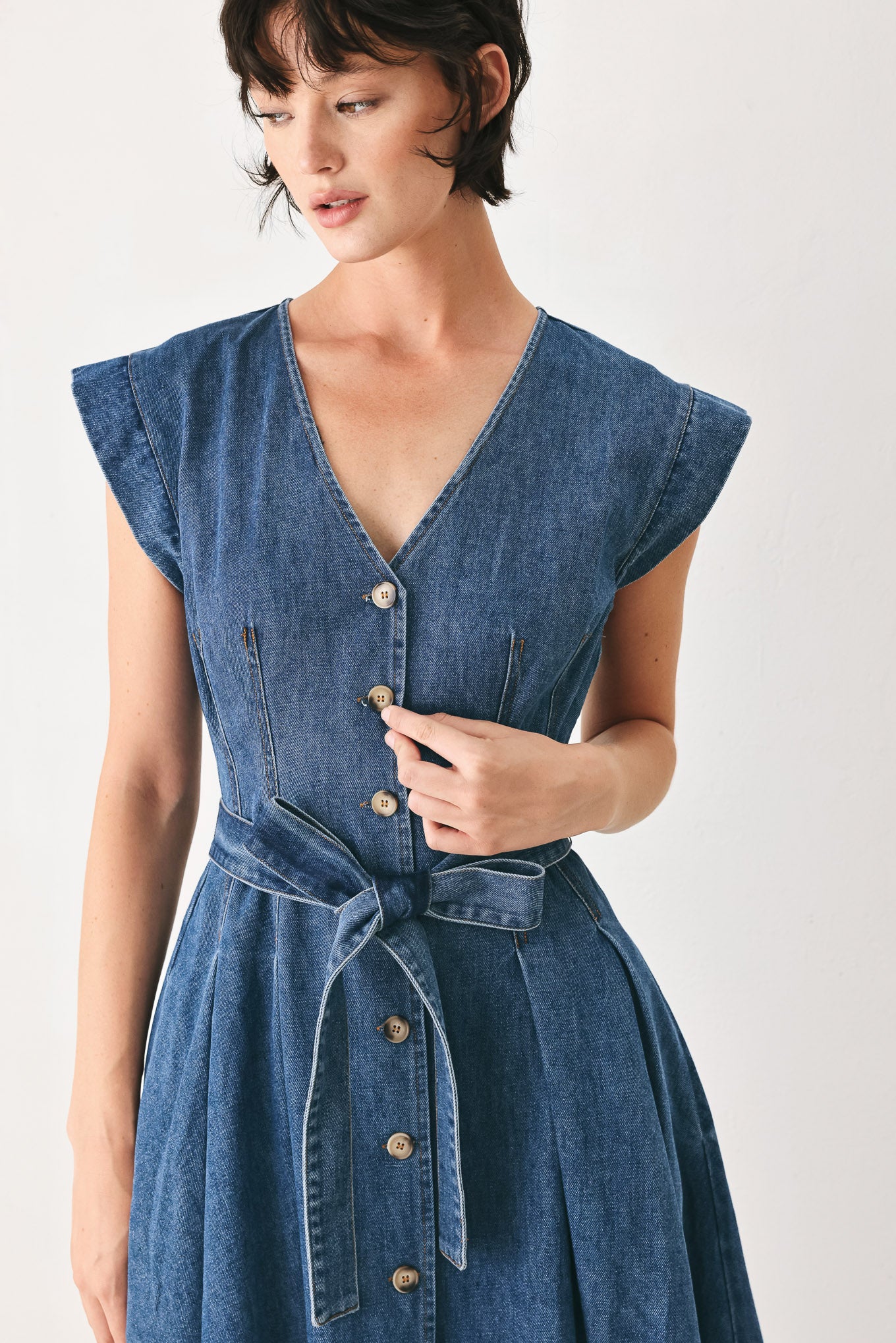 Woman wearing a short sleeve blue denim midi dress with V neckline, front button down, corset waist, self sash tie and full skirt | FREEMARKET