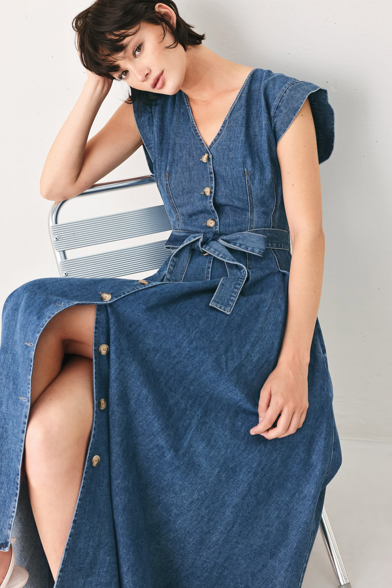 Woman wearing a short sleeve blue denim midi dress with V neckline, front button down, corset waist, self sash tie and full skirt | FREEMARKET