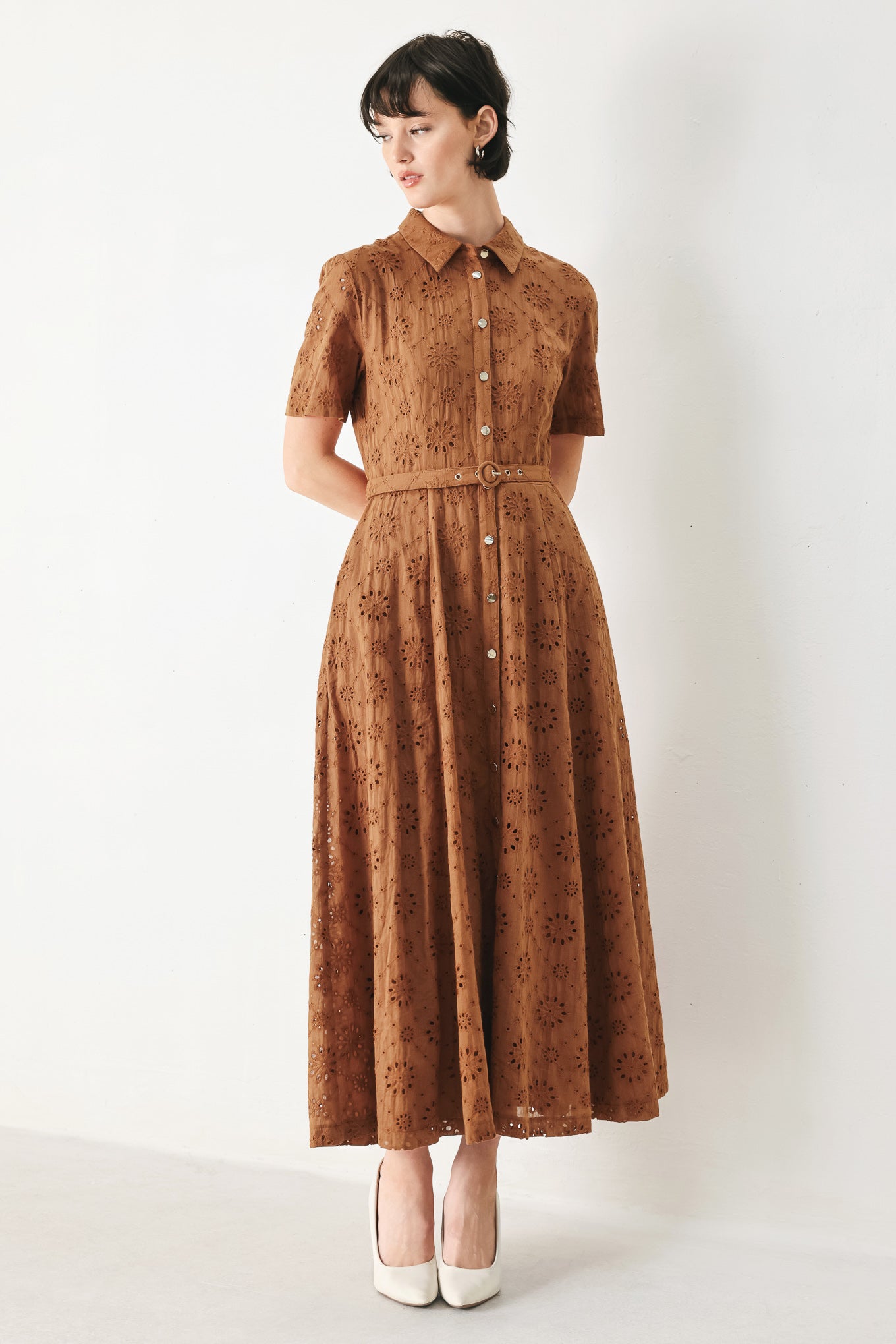 Woman wearing a camel colored eyelet midi dress featuring collar, short sleeve, front button closure, self belt, side pockets and full skirt | FREEMARKET