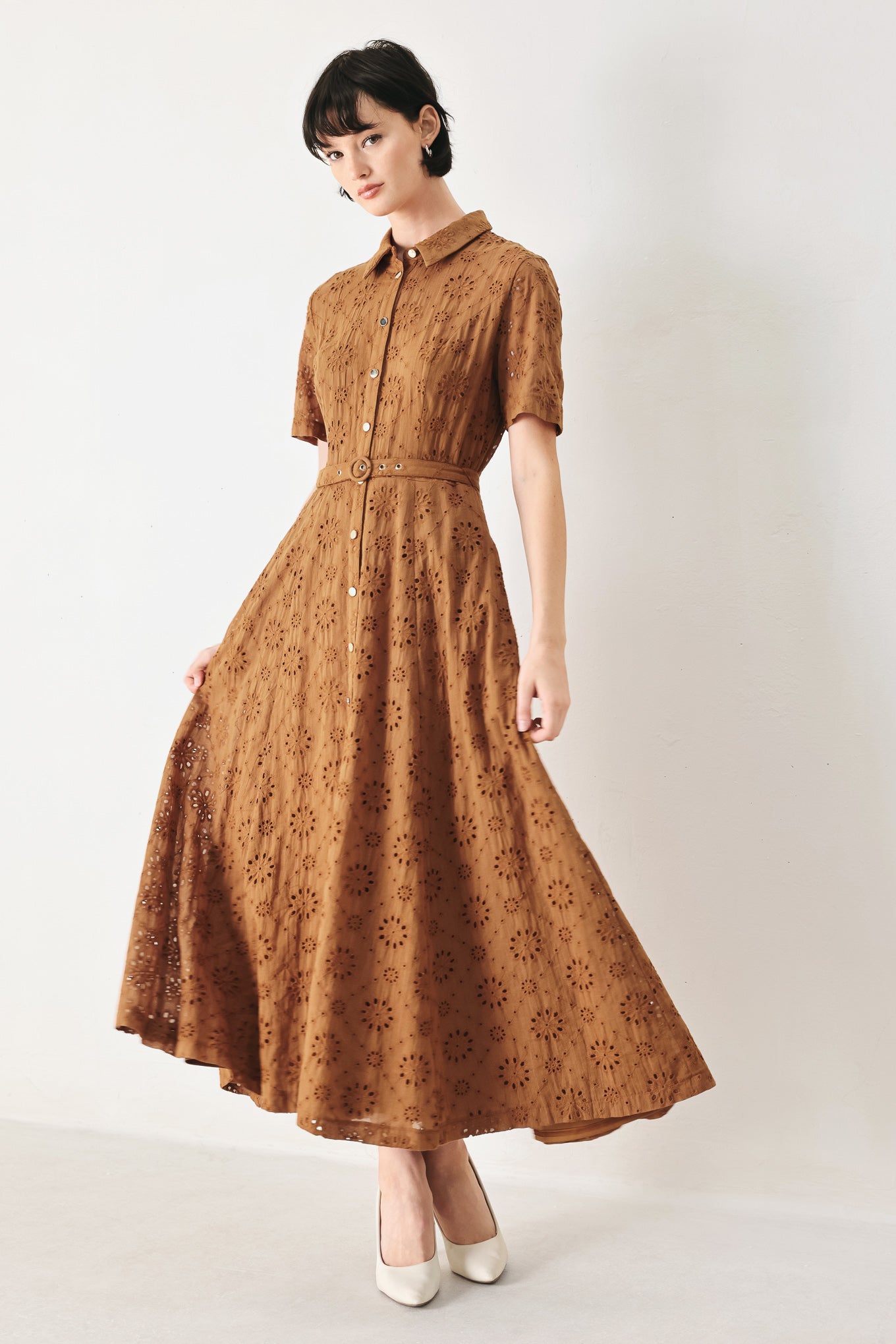 Woman wearing a camel colored eyelet midi dress featuring collar, short sleeve, front button closure, self belt, side pockets and full skirt | FREEMARKET