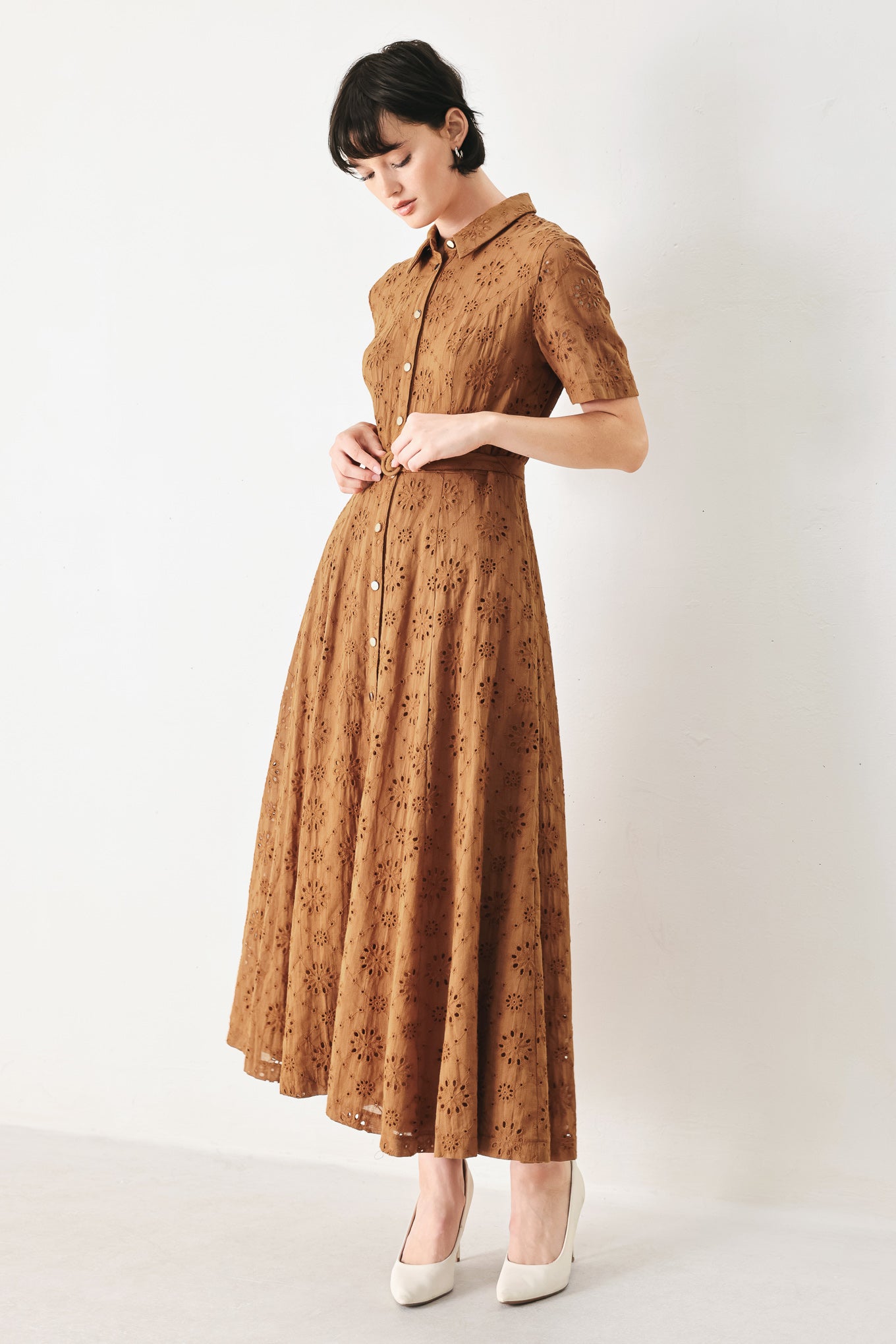 Woman wearing a camel colored eyelet midi dress featuring collar, short sleeve, front button closure, self belt, side pockets and full skirt | FREEMARKET