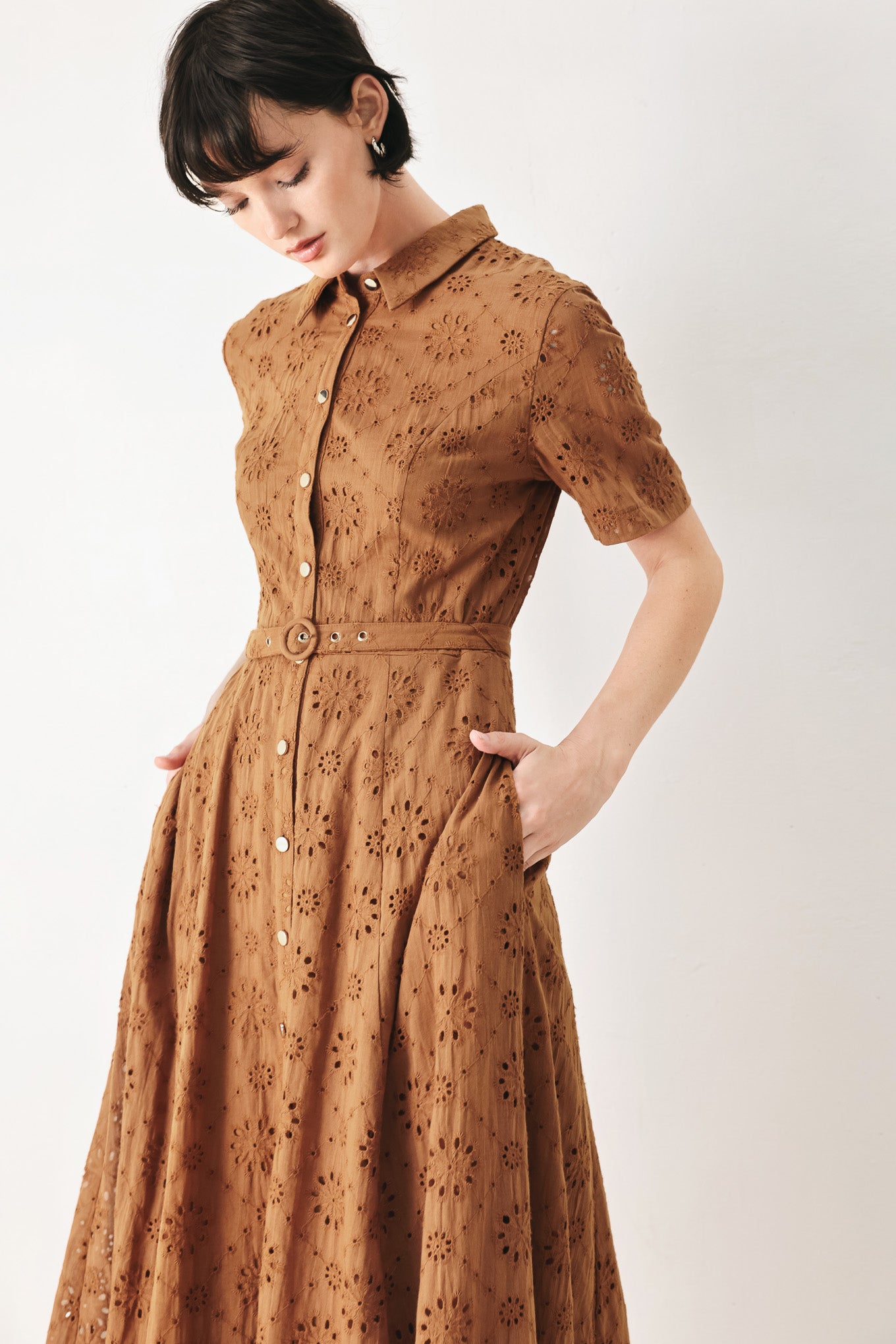 Woman wearing a camel colored eyelet midi dress featuring collar, short sleeve, front button closure, self belt, side pockets and full skirt | FREEMARKET