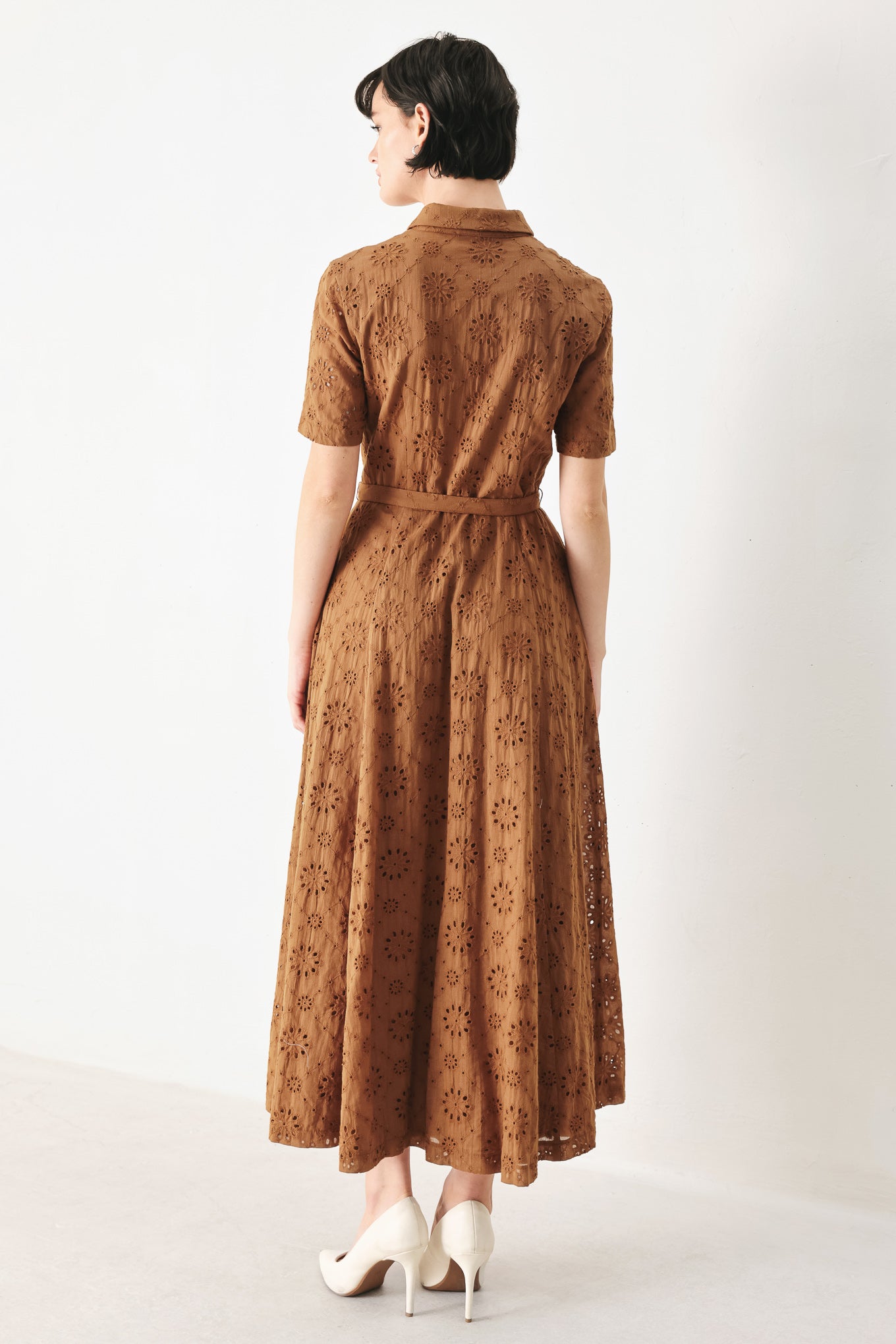 Woman wearing a camel colored eyelet midi dress featuring collar, short sleeve, front button closure, self belt, side pockets and full skirt | FREEMARKET