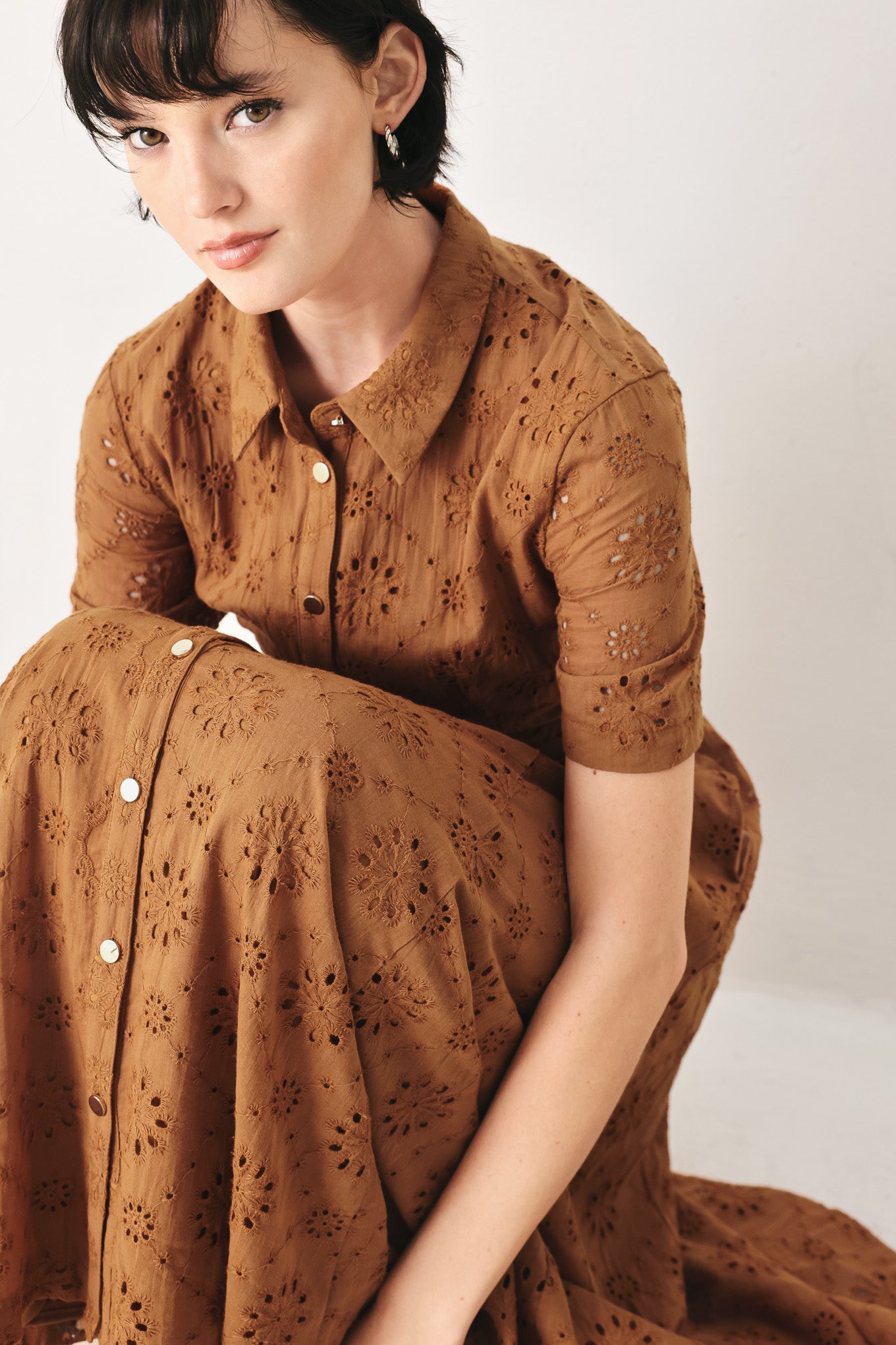 Woman wearing a camel colored eyelet midi dress featuring collar, short sleeve, front button closure, self belt, side pockets and full skirt | FREEMARKET