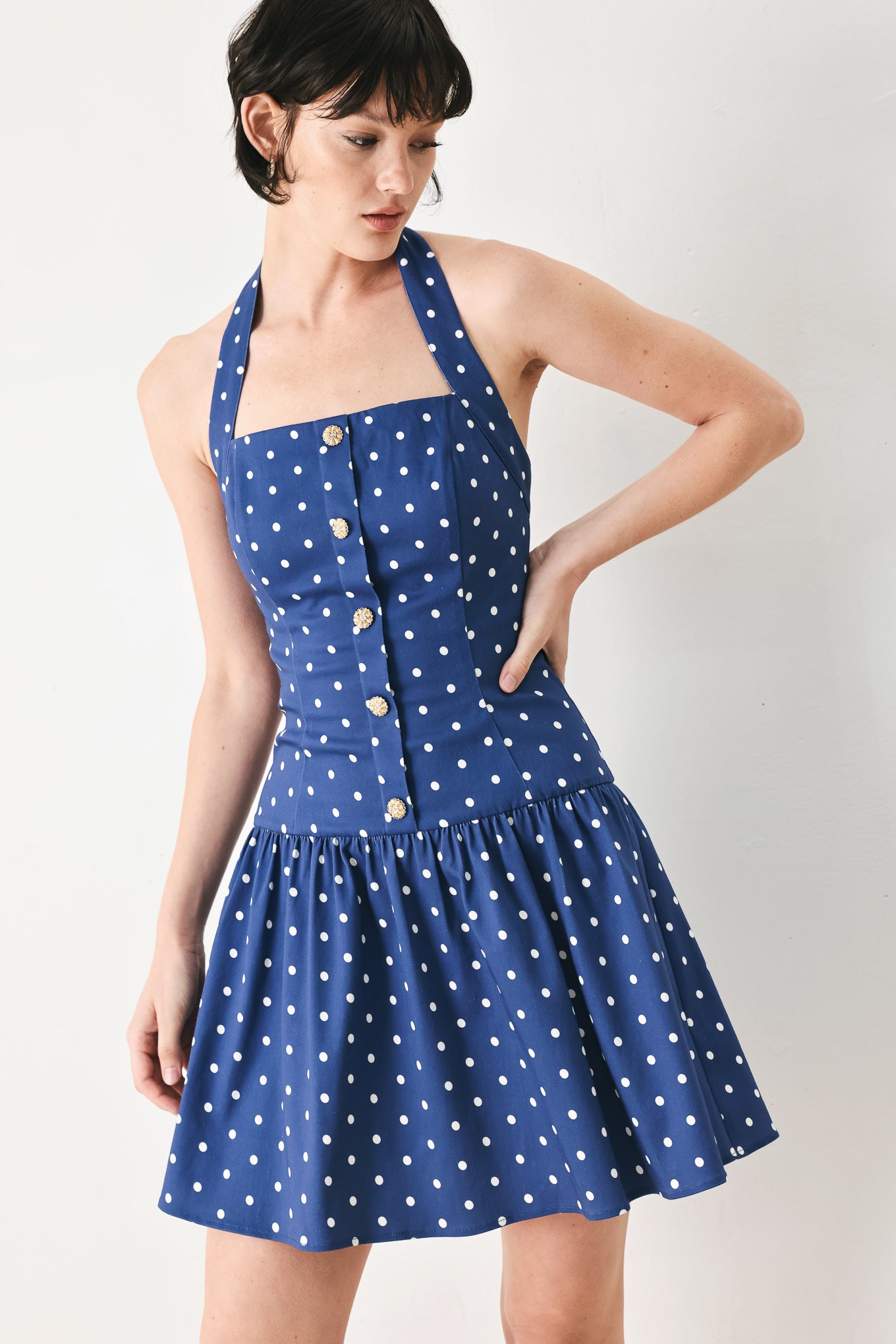Woman wearing a blue polka dot mini dress featuring straight neckline with halter strap, drop waist and bare back with smocking zipper closure | FREEMARKET