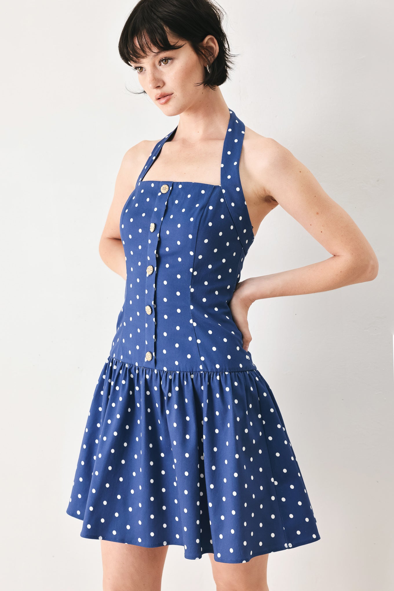 Woman wearing a blue polka dot mini dress featuring straight neckline with halter strap, drop waist and bare back with smocking zipper closure | FREEMARKET