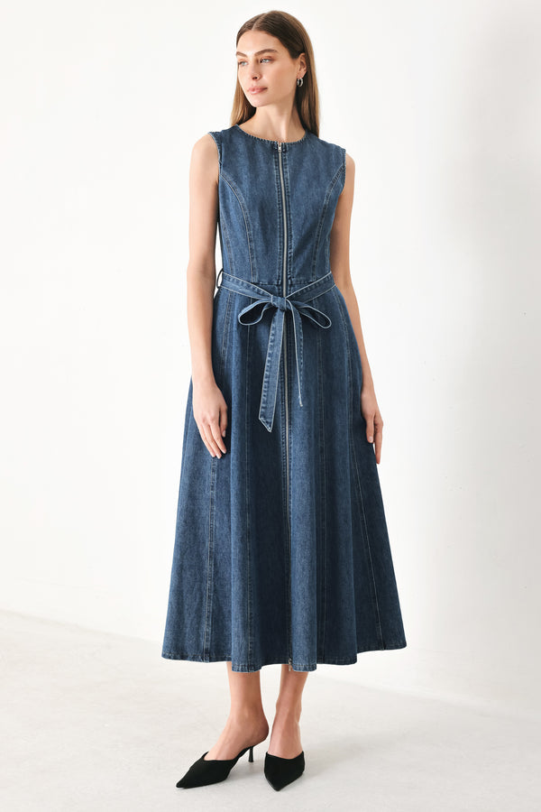 Woman wearing a blue denim midi dress featuring round neckline, sleeveless, self sash tie, circle skirt, side pockets and front zipper closure | FREEMARKET | Flying Tomato