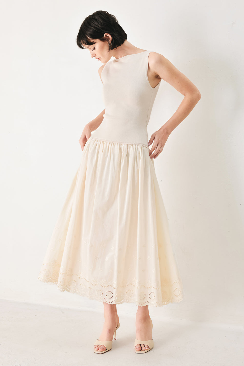 Woman wearing a sleeveless ivory midi dress featuring sweater knit top with round neckline, drop waist, woven eyelet skirt, U back neck and cut out at waist | FREEMARKET