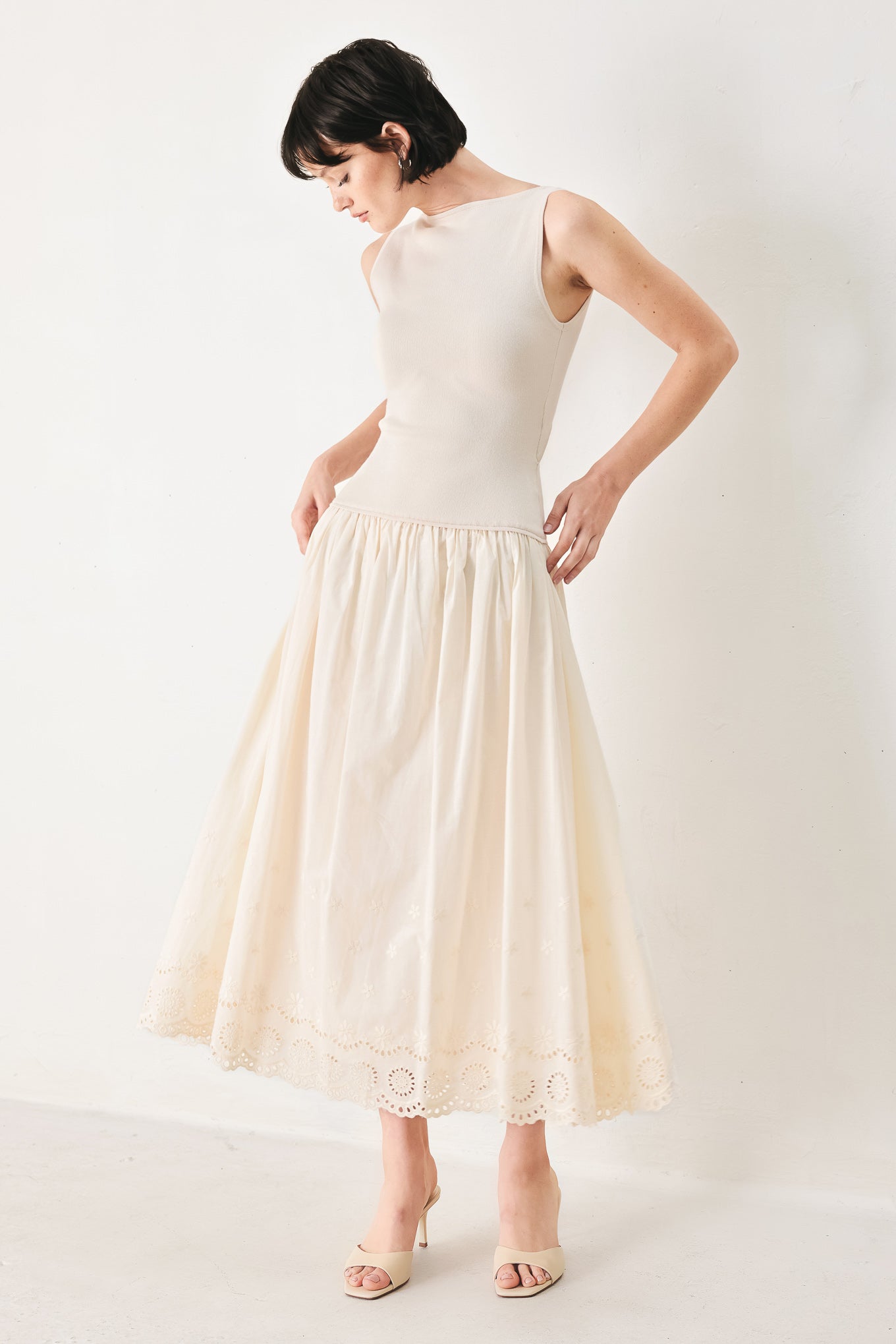 Woman wearing a sleeveless ivory midi dress featuring sweater knit top with round neckline, drop waist, woven eyelet skirt, U back neck and cut out at waist | FREEMARKET