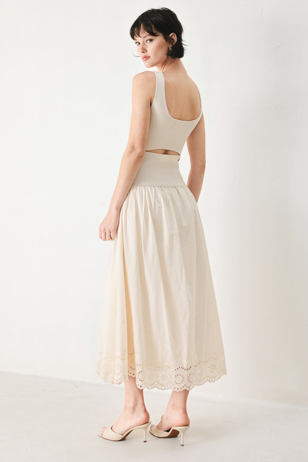 Woman wearing a sleeveless ivory midi dress featuring sweater knit top with round neckline, drop waist, woven eyelet skirt, U back neck and cut out at waist | FREEMARKET