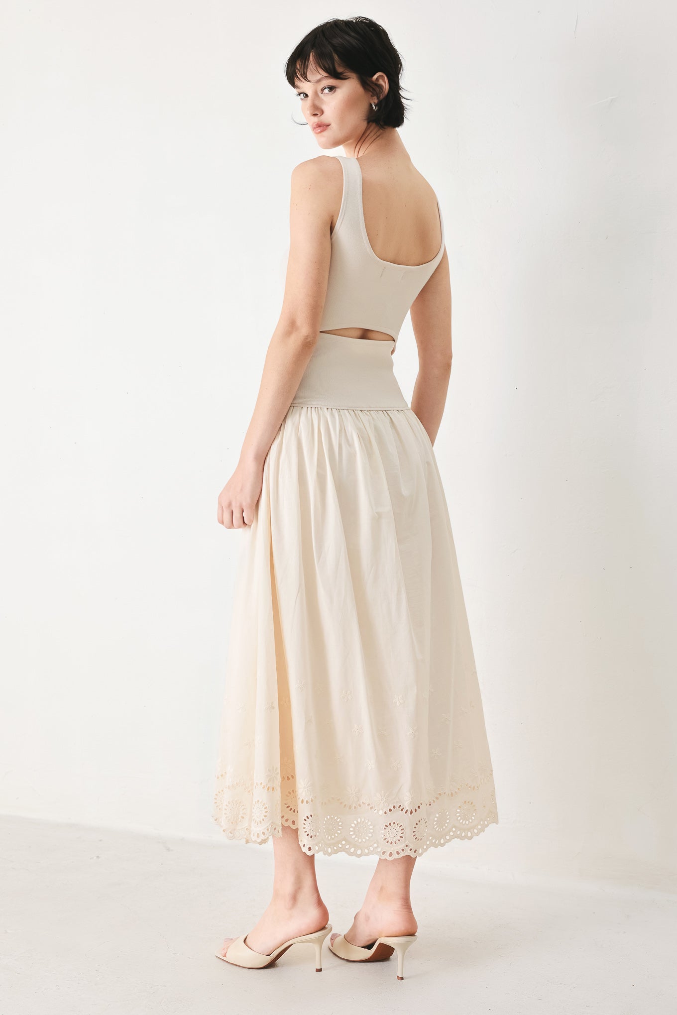 Woman wearing a sleeveless ivory midi dress featuring sweater knit top with round neckline, drop waist, woven eyelet skirt, U back neck and cut out at waist | FREEMARKET