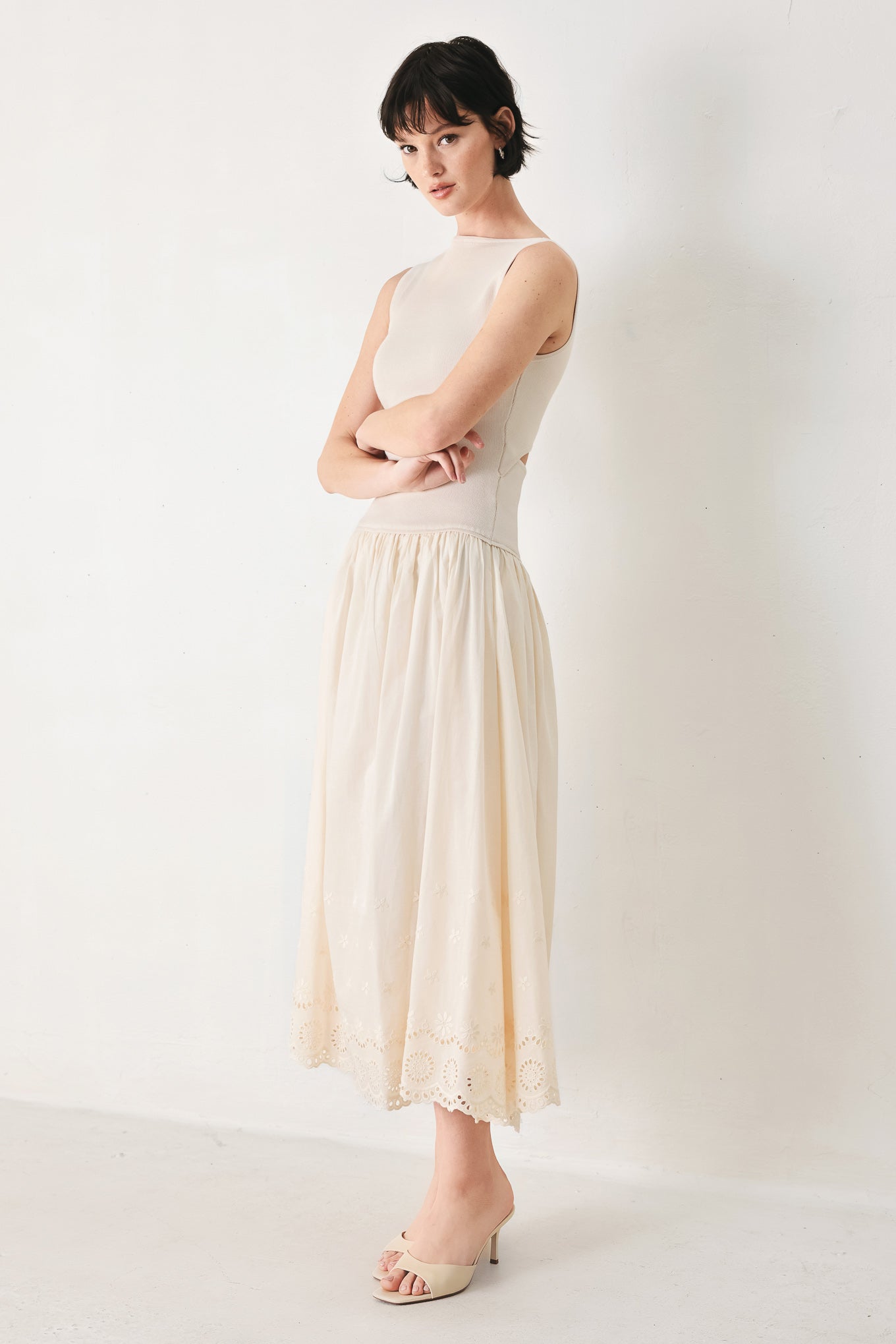 Woman wearing a sleeveless ivory midi dress featuring sweater knit top with round neckline, drop waist, woven eyelet skirt, U back neck and cut out at waist | FREEMARKET