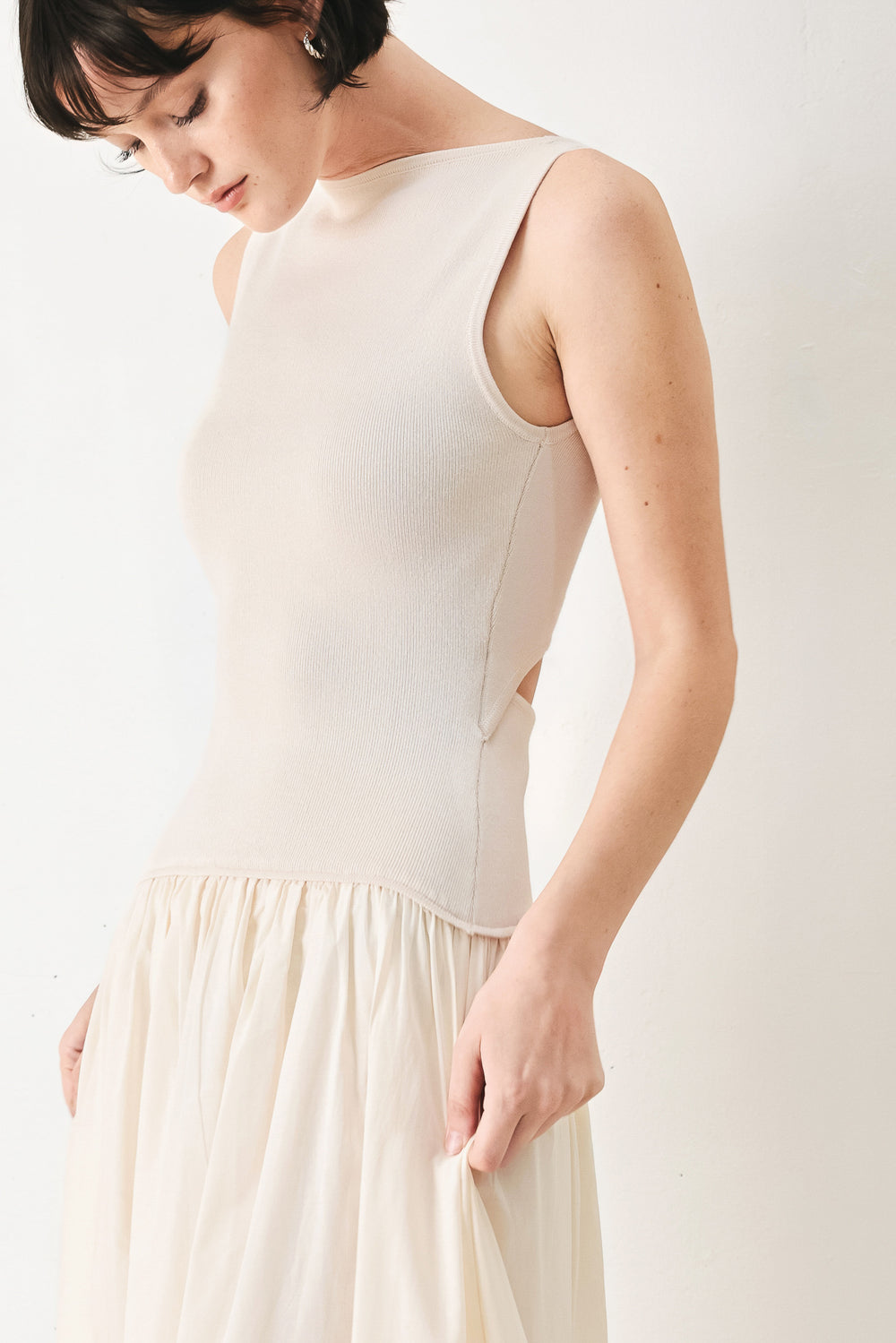 Woman wearing a sleeveless ivory midi dress featuring sweater knit top with round neckline, drop waist, woven eyelet skirt, U back neck and cut out at waist | FREEMARKET