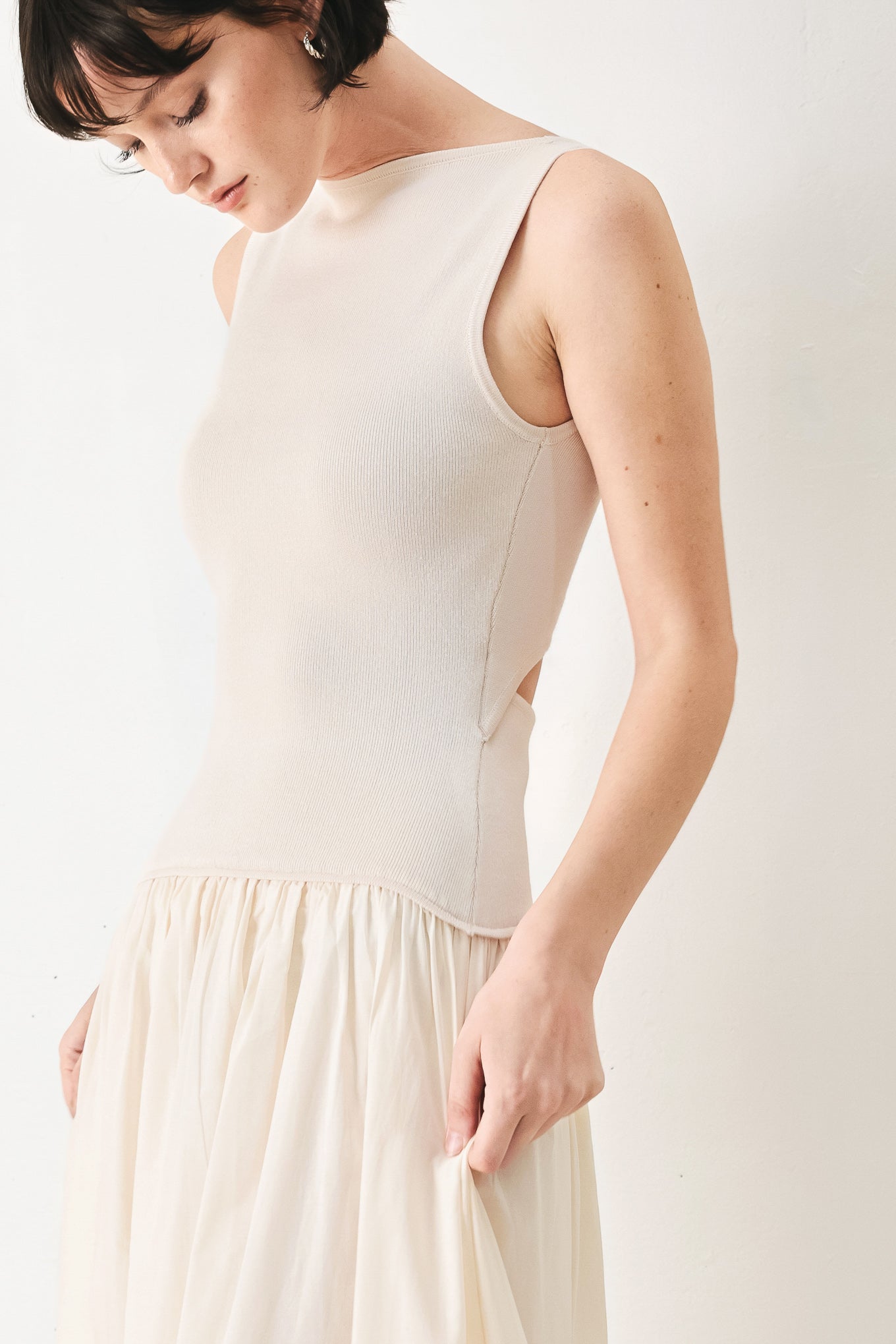 Woman wearing a sleeveless ivory midi dress featuring sweater knit top with round neckline, drop waist, woven eyelet skirt, U back neck and cut out at waist | FREEMARKET