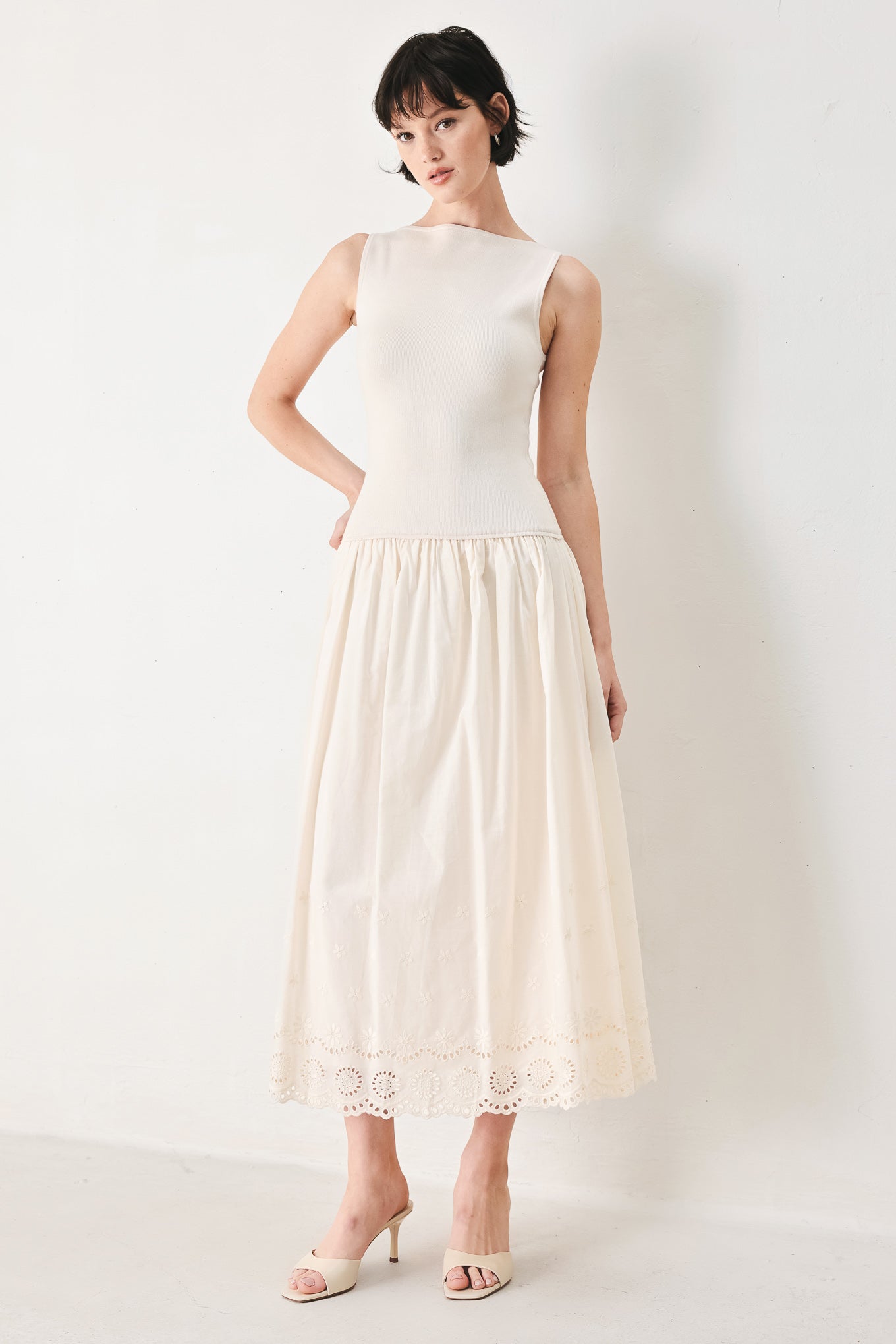 Woman wearing a sleeveless ivory midi dress featuring sweater knit top with round neckline, drop waist, woven eyelet skirt, U back neck and cut out at waist | FREEMARKET