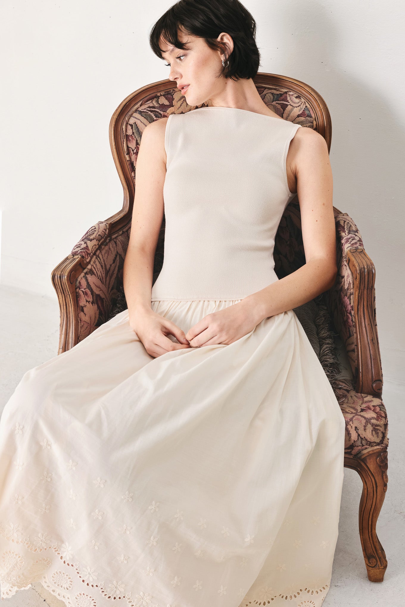 Woman wearing a sleeveless ivory midi dress featuring sweater knit top with round neckline, drop waist, woven eyelet skirt, U back neck and cut out at waist | FREEMARKET