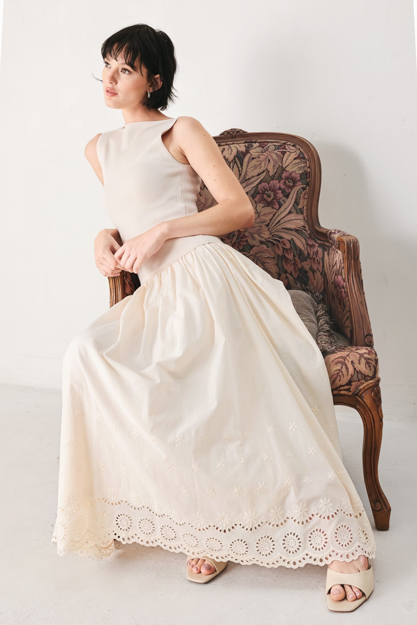 Woman wearing a sleeveless ivory midi dress featuring sweater knit top with round neckline, drop waist, woven eyelet skirt, U back neck and cut out at waist | FREEMARKET