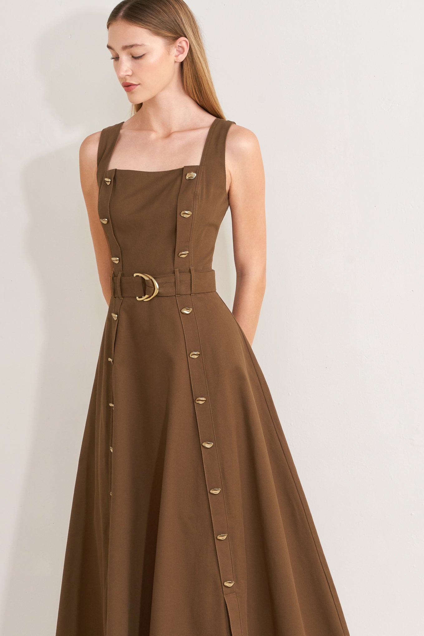 Woman wearing a brown solid woven midi dress featuring straight neckline, straps, button down detail, self belt, circle skirt and back zipper closure with a belt on a plain background | FREEMARKET | Flying Tomato