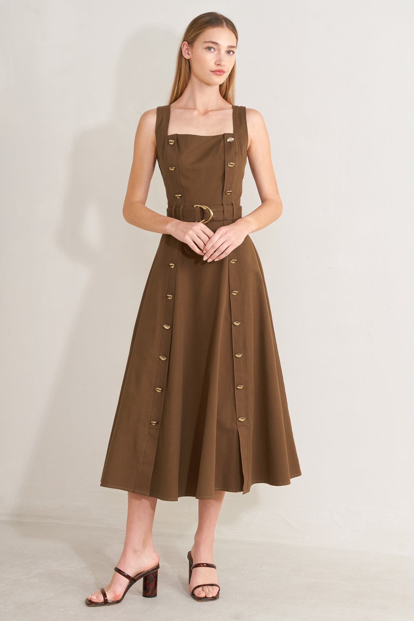 Woman wearing a brown solid woven midi dress featuring straight neckline, straps, button down detail, self belt, circle skirt and back zipper closure with a belt on a plain background | FREEMARKET | Flying Tomato