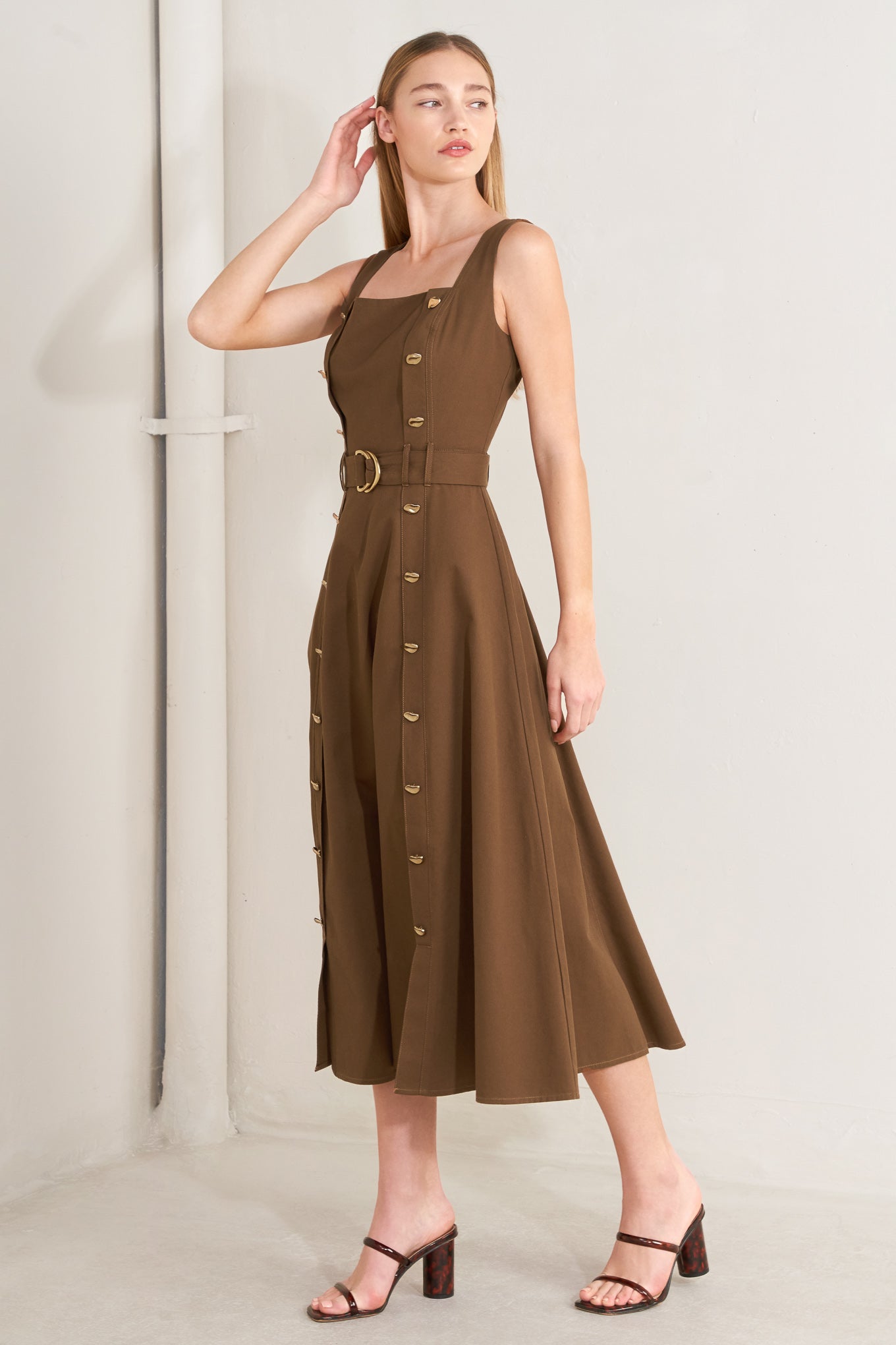 Woman wearing a brown solid woven midi dress featuring straight neckline, straps, button down detail, self belt, circle skirt and back zipper closure with a belt on a plain background | FREEMARKET | Flying Tomato