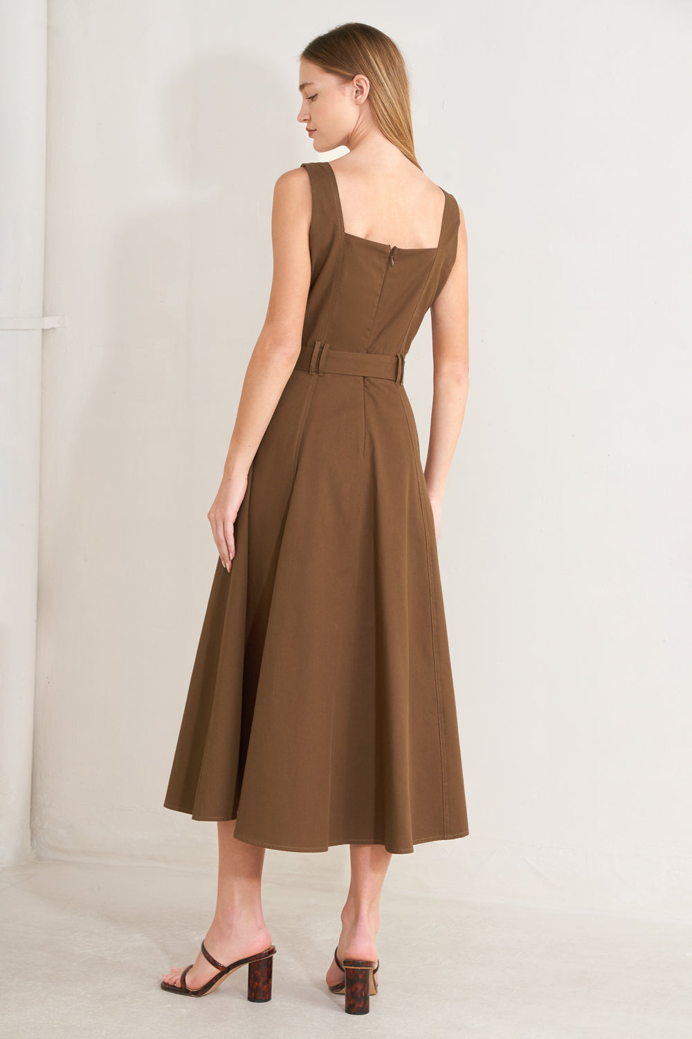 Woman wearing a brown solid woven midi dress featuring straight neckline, straps, button down detail, self belt, circle skirt and back zipper closure with a belt on a plain background | FREEMARKET | Flying Tomato