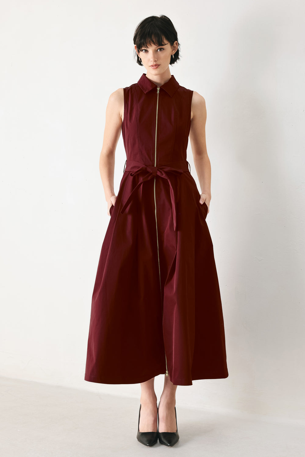Woman wearing a burgundy red woven midi dress featuring collar, sleeveless, front zipper closure, self sash tie, pockets and full skirt | FREEMARKET