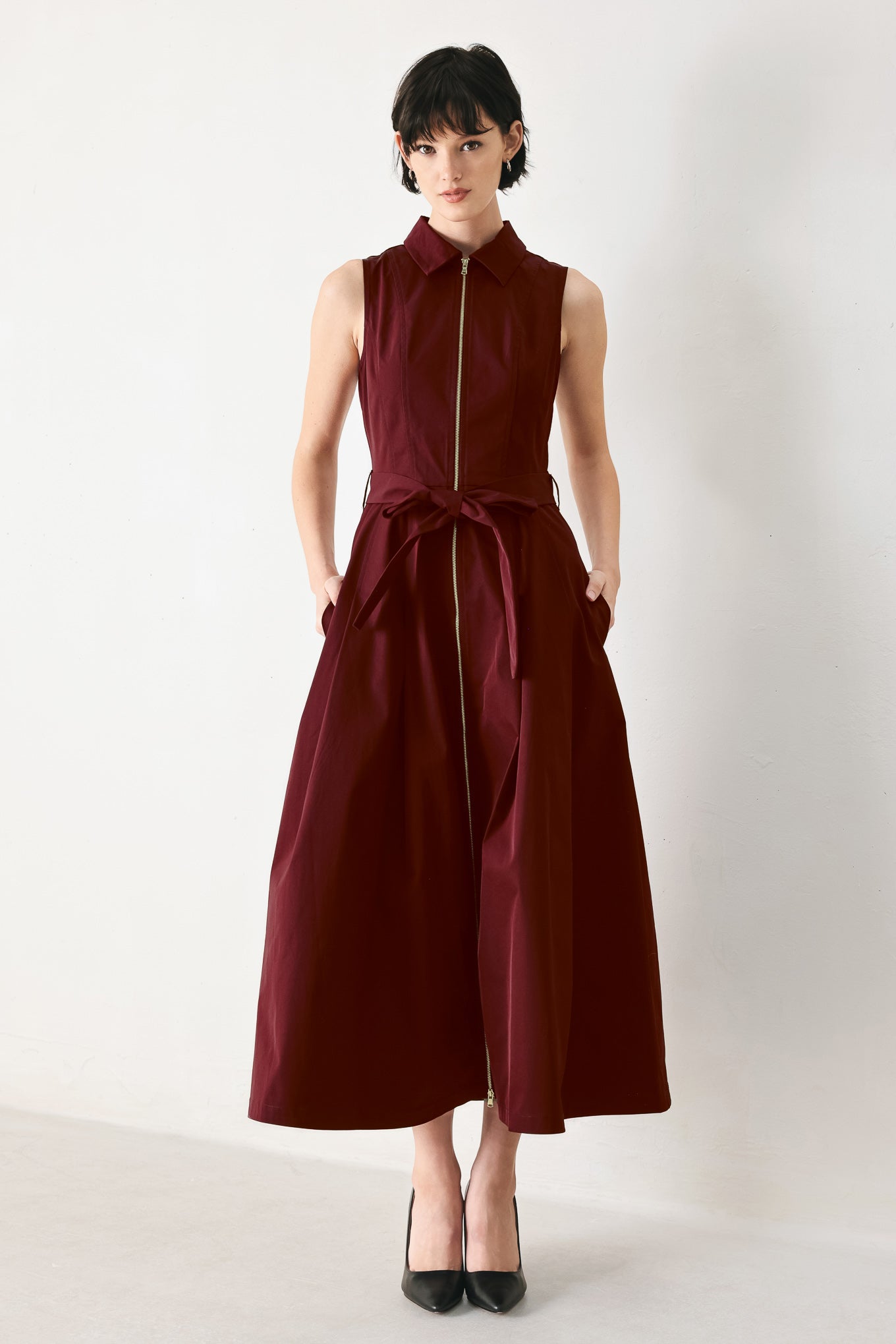 Woman wearing a burgundy red woven midi dress featuring collar, sleeveless, front zipper closure, self sash tie, pockets and full skirt | FREEMARKET