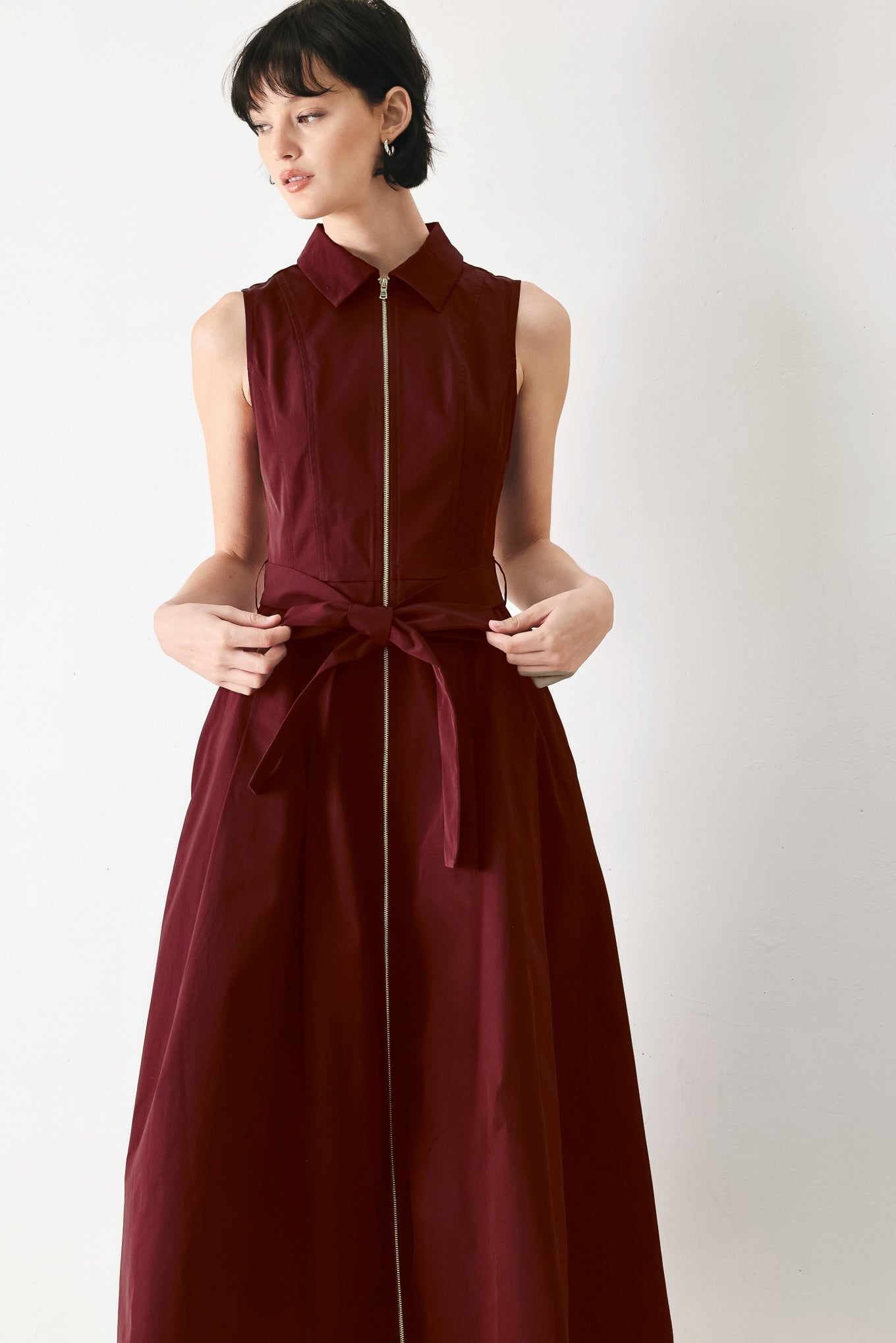 Woman wearing a burgundy red woven midi dress featuring collar, sleeveless, front zipper closure, self sash tie, pockets and full skirt | FREEMARKET