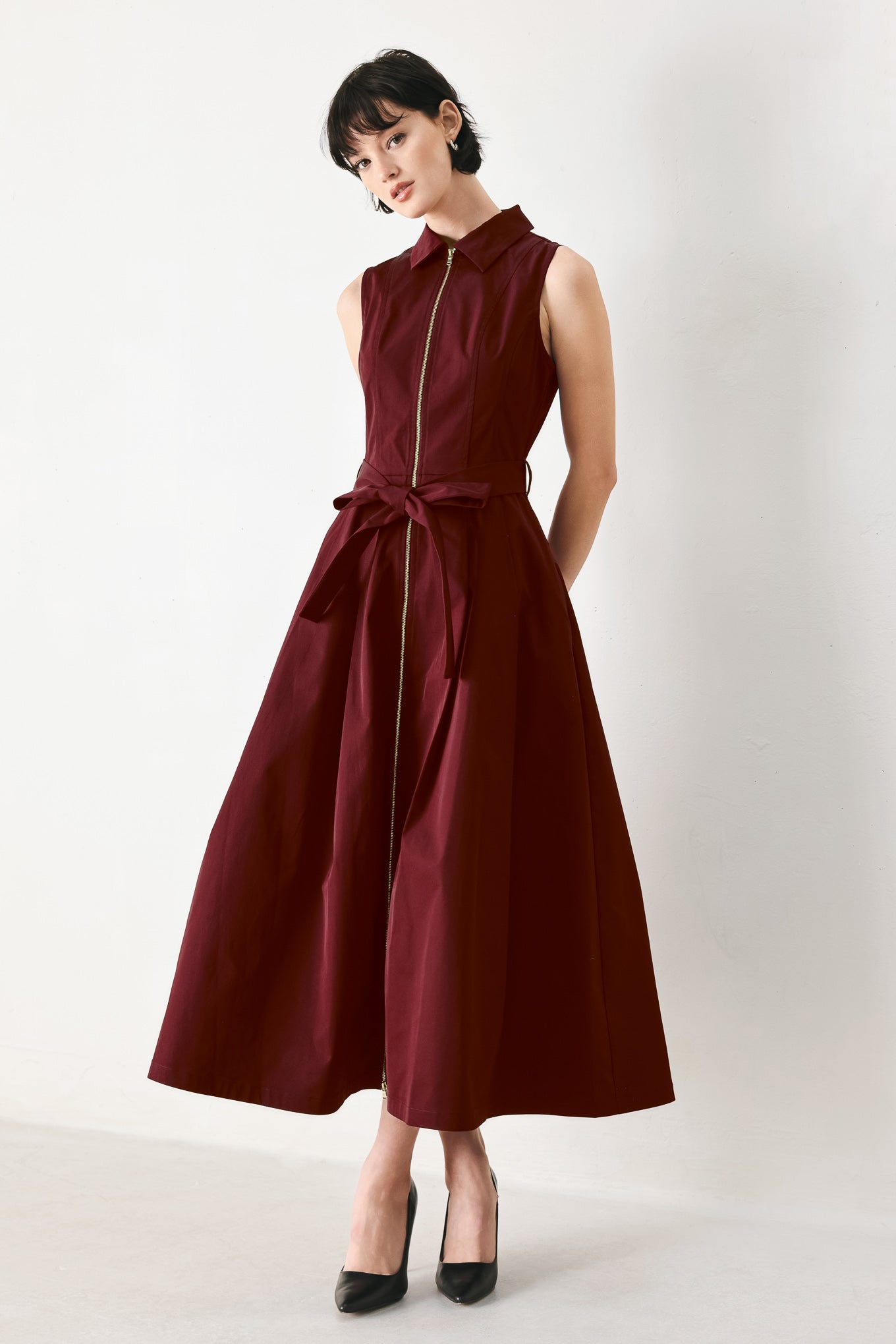 Woman wearing a burgundy red woven midi dress featuring collar, sleeveless, front zipper closure, self sash tie, pockets and full skirt | FREEMARKET